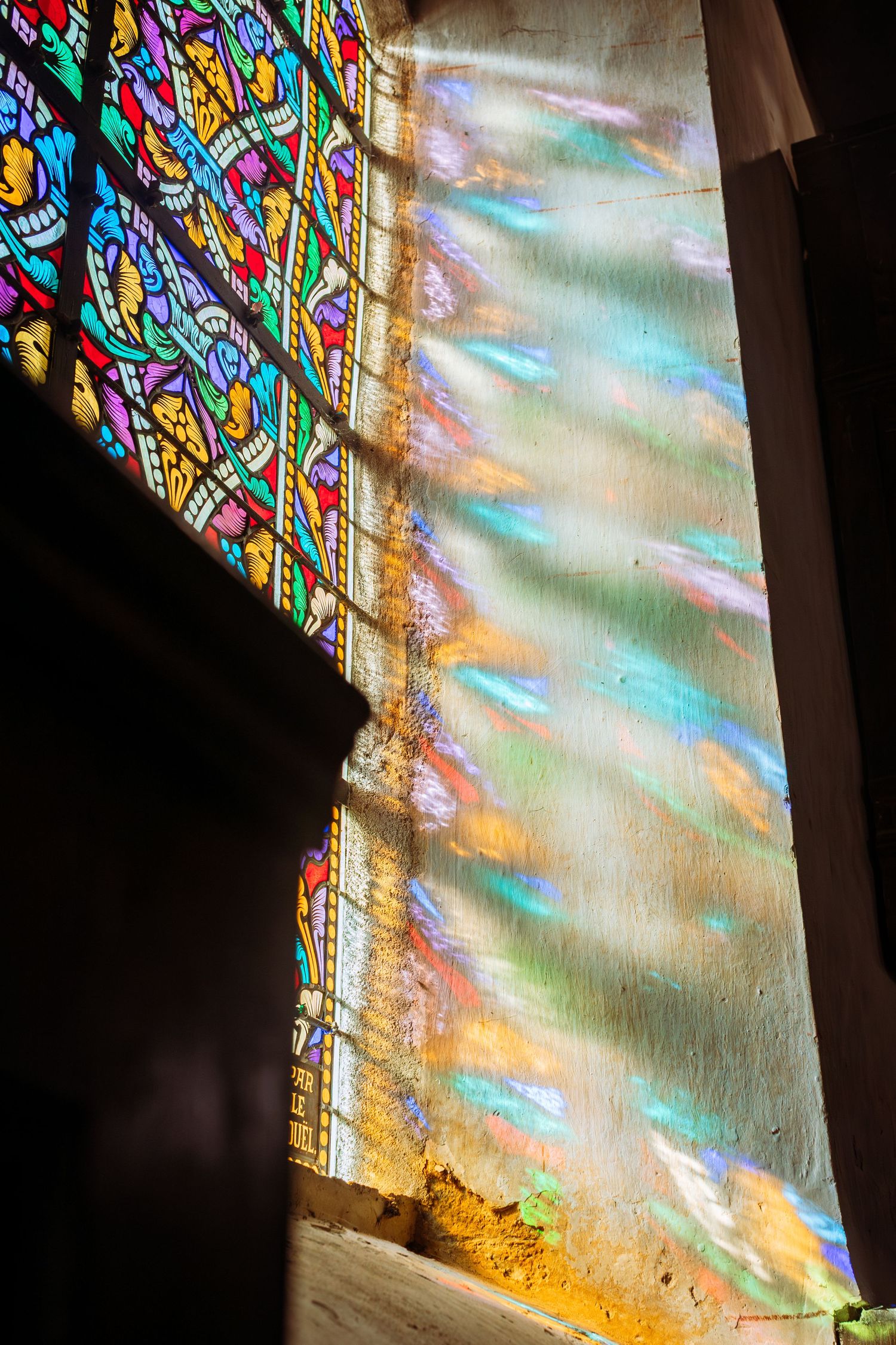 Colorful light streams through stained glass window creating rainbow prism effect on church wall.