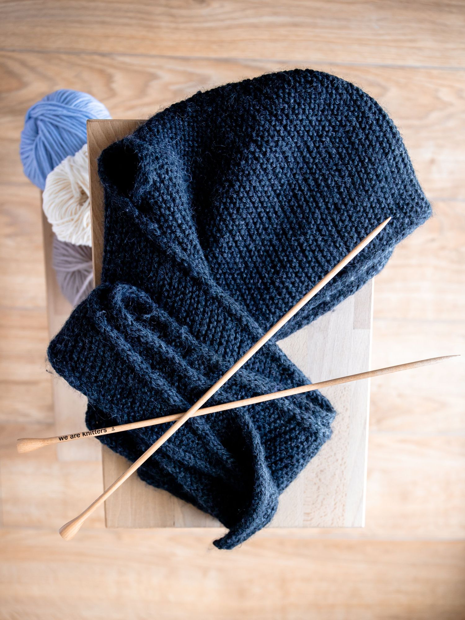 Navy blue knitted project with knitting needles and yarn balls on wooden surface.