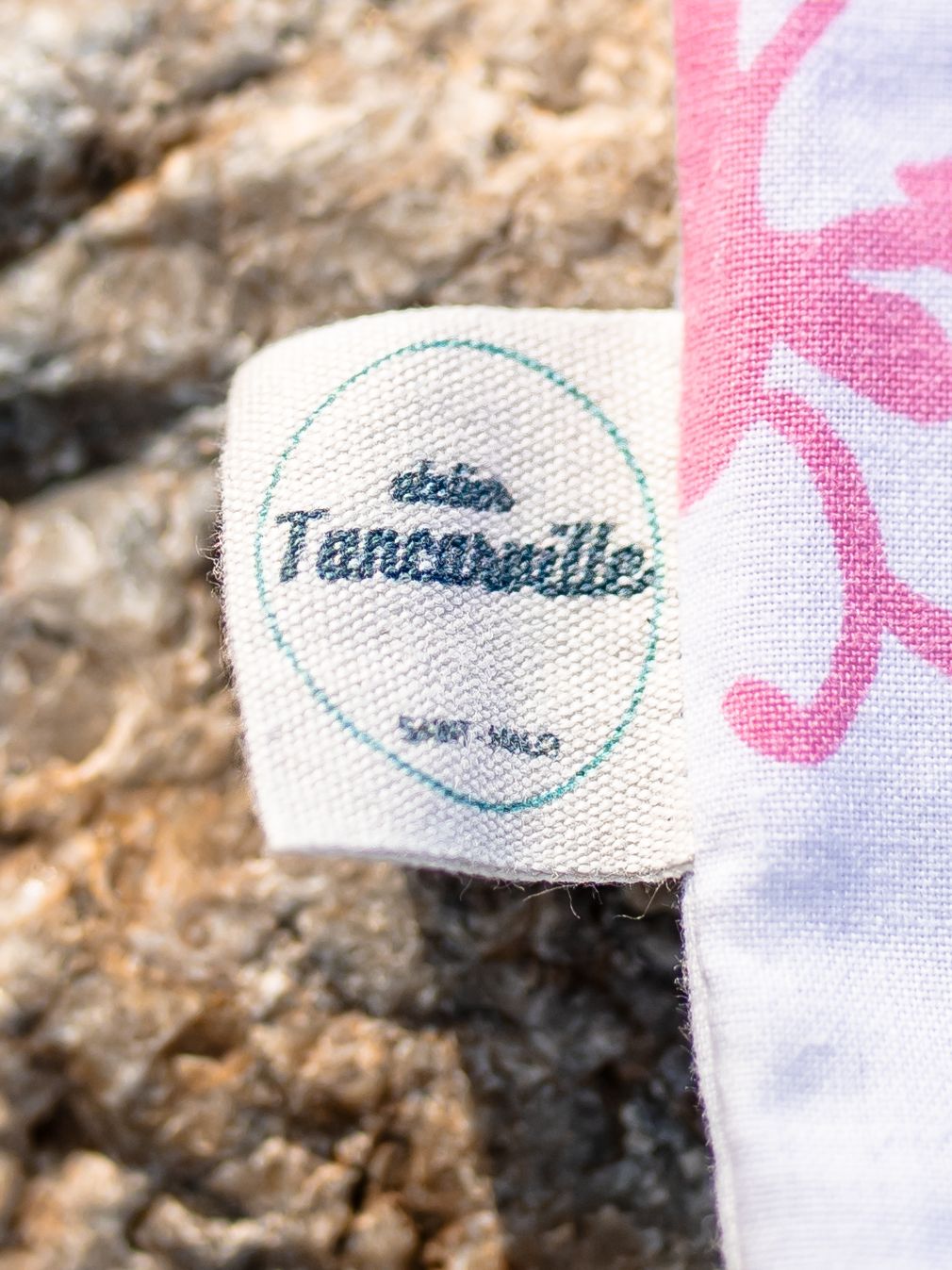 Close-up view of embroidered fabric labels showing brand text details against a white and pink textured background.