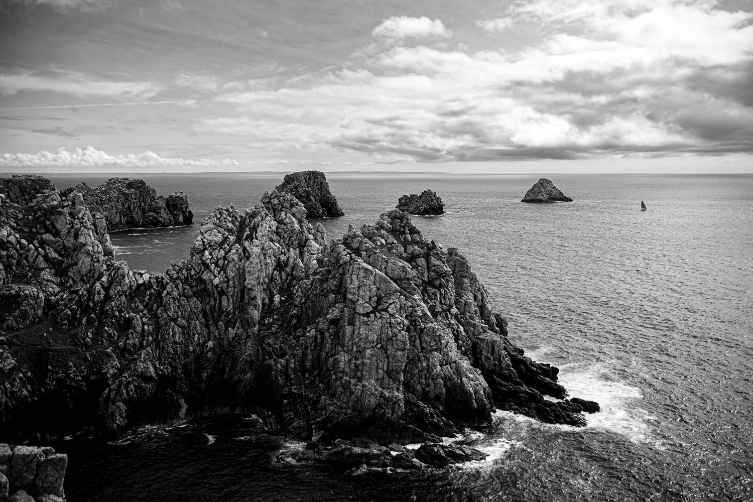 Dramatic black and white coastal landscape with rugged cliffs and rock formations jutting into a misty ocean.