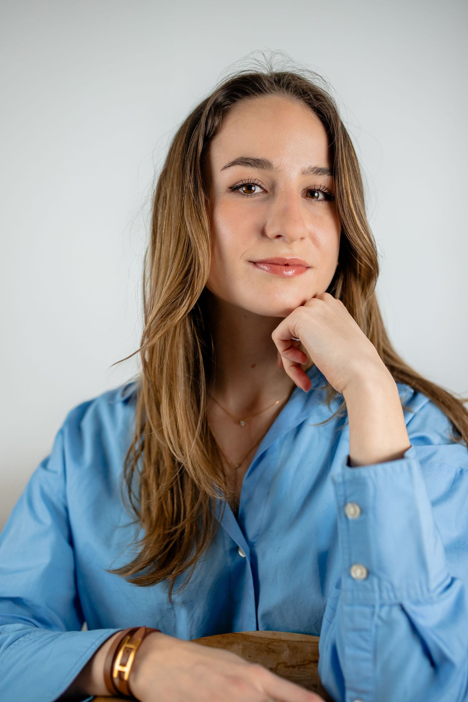 Portrait of someone in a blue button-down shirt with long wavy hair against a light background.