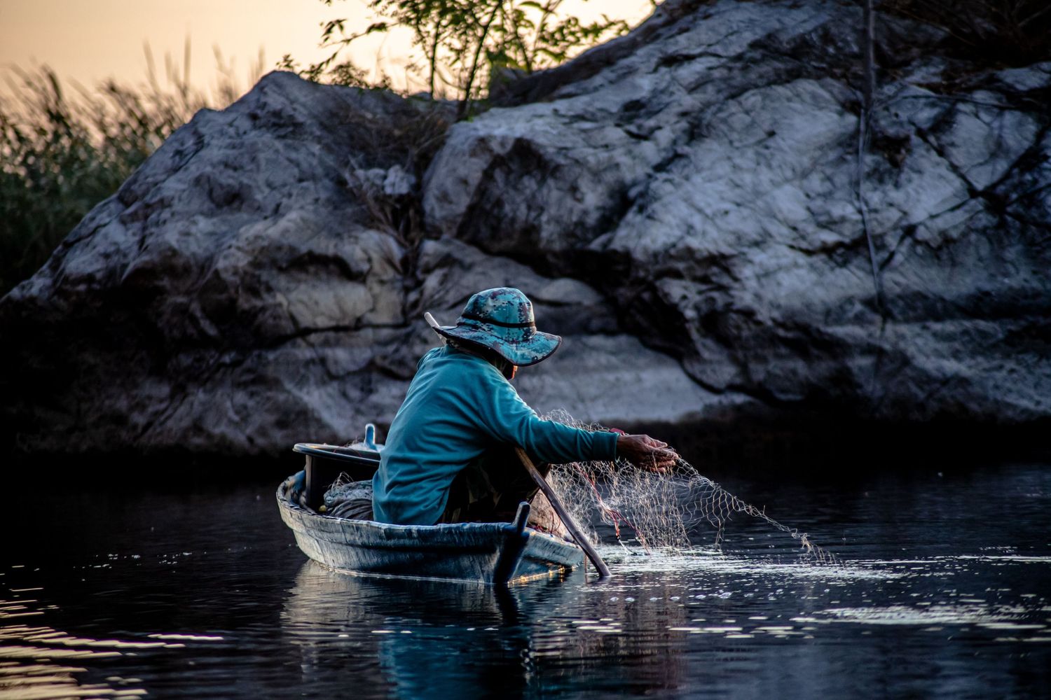 Cast net fishing scene against rocky backdrop in evening light.