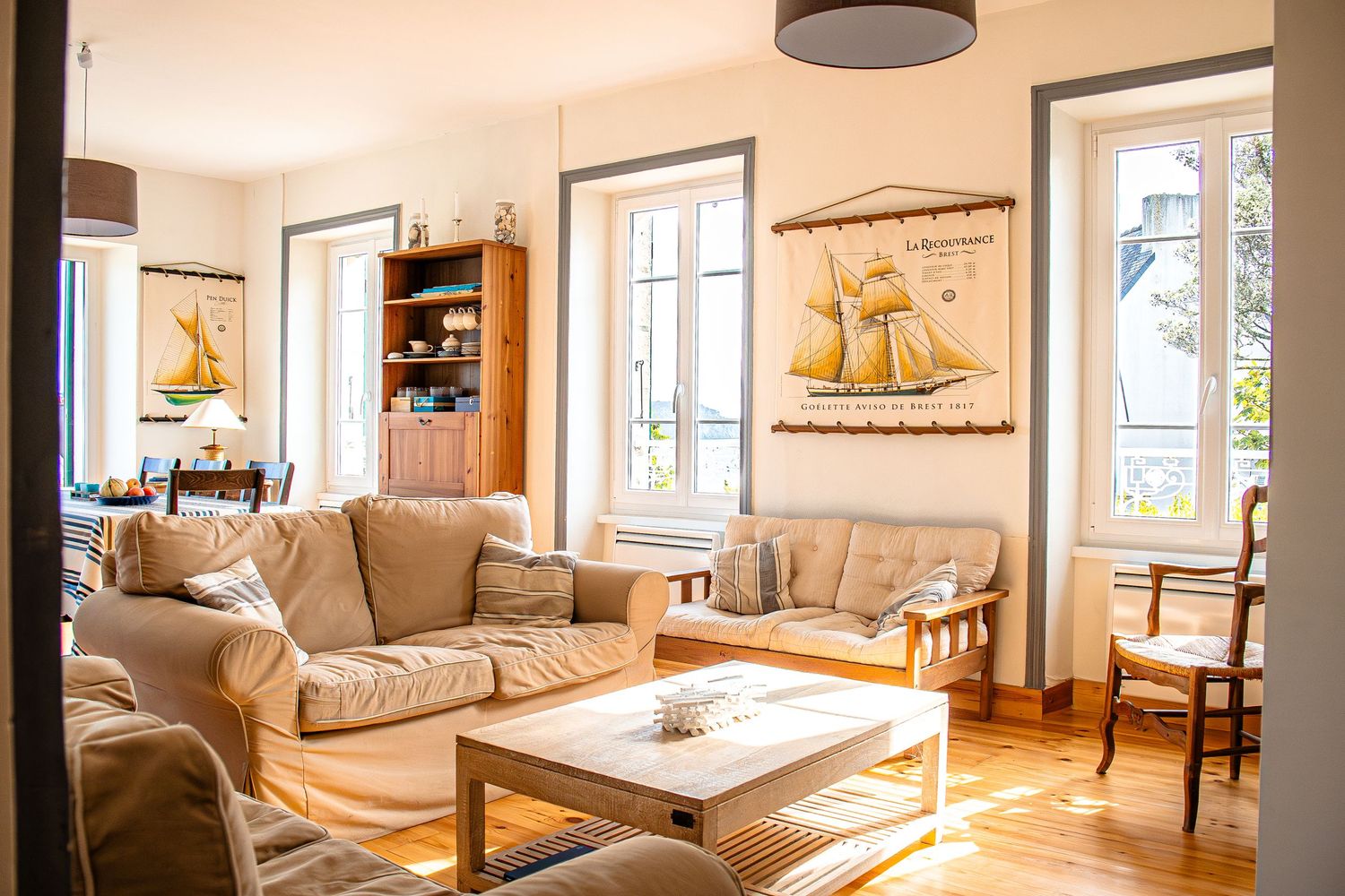 Modern open concept living room with beige sofas, large windows, and hardwood floors in a bright, airy space.