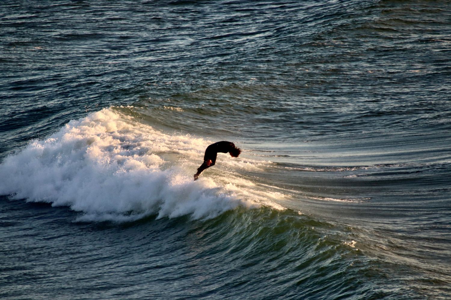Surfer rides the crest of a wave during golden hour.