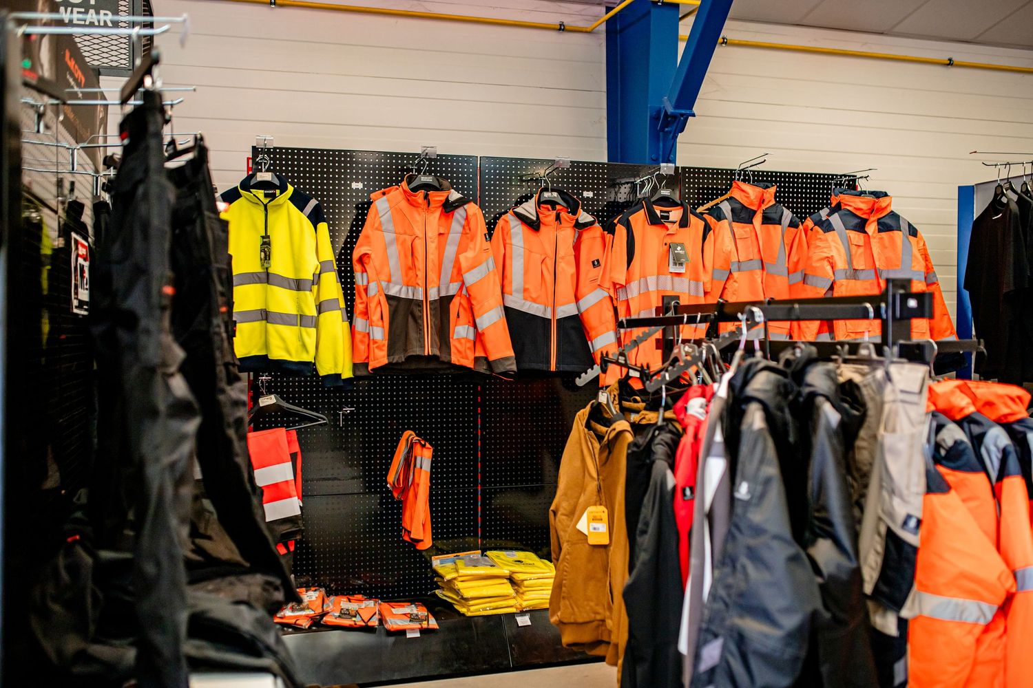 Retail display of high-visibility safety workwear including orange and yellow jackets.