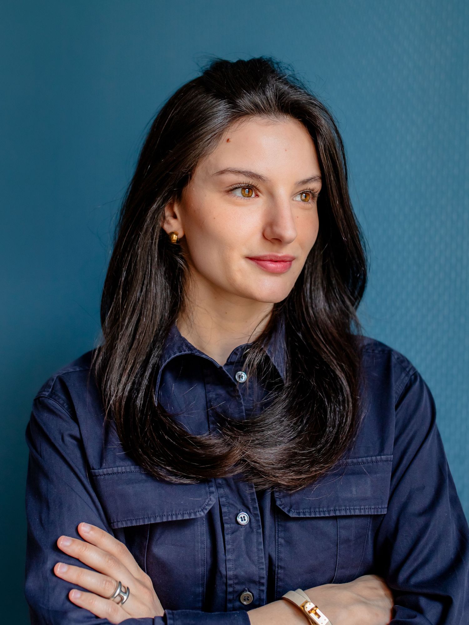 Studio portrait in navy shirt against blue backdrop with crossed arms and confident pose.