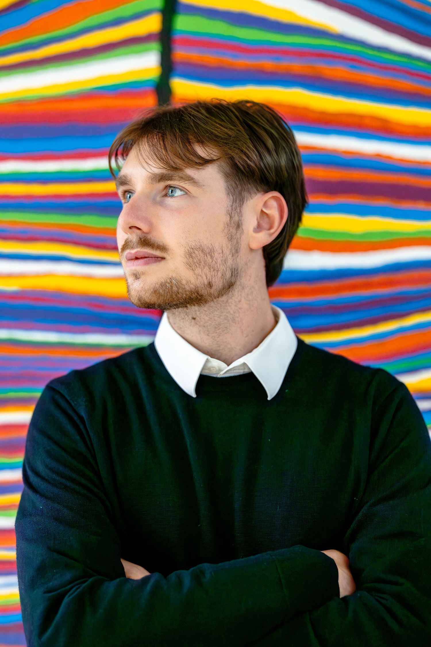 Professional portrait with navy sweater and white collar against vibrant striped background.