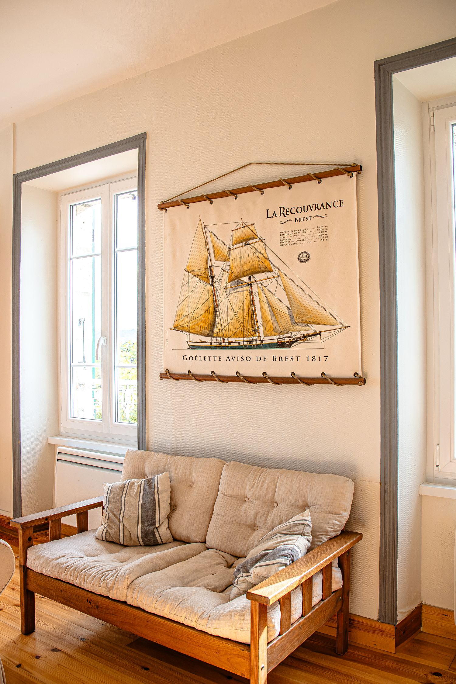 A panoramic view of a modern living room with wooden futon sofa, nautical wall art, and model sailing ship decor.