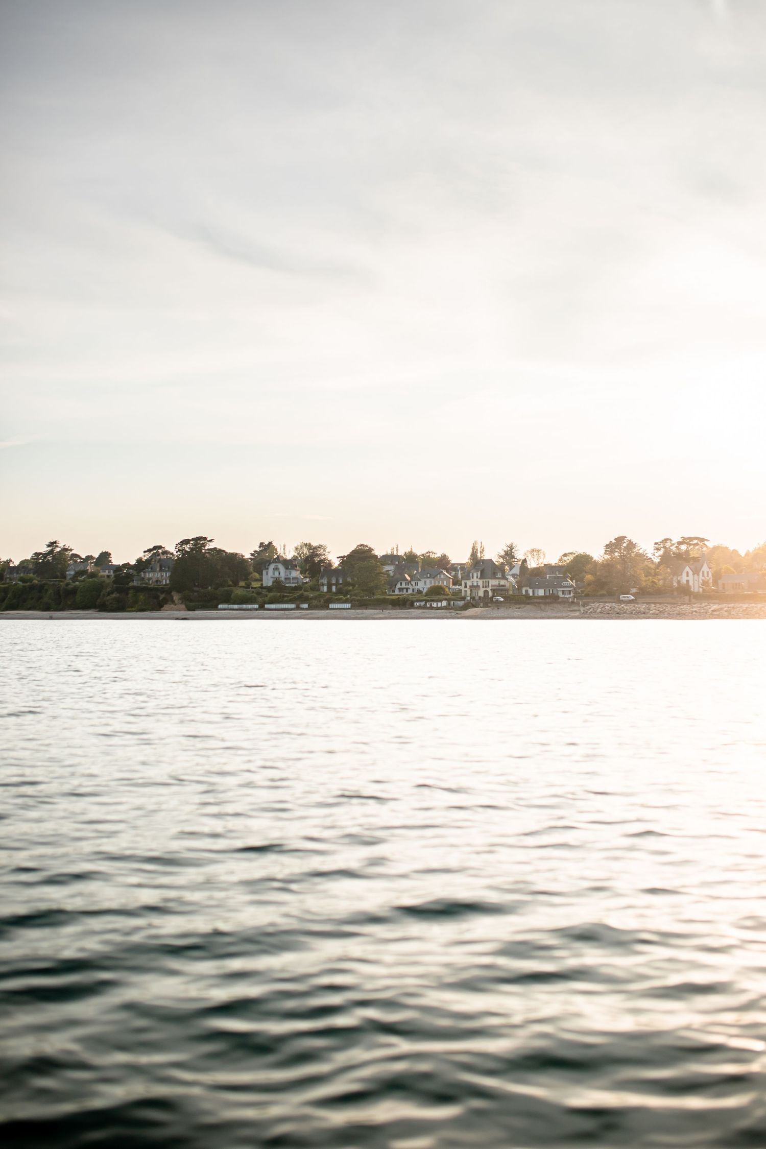 Calm ocean waters at sunset with coastal homes visible along the distant shoreline.