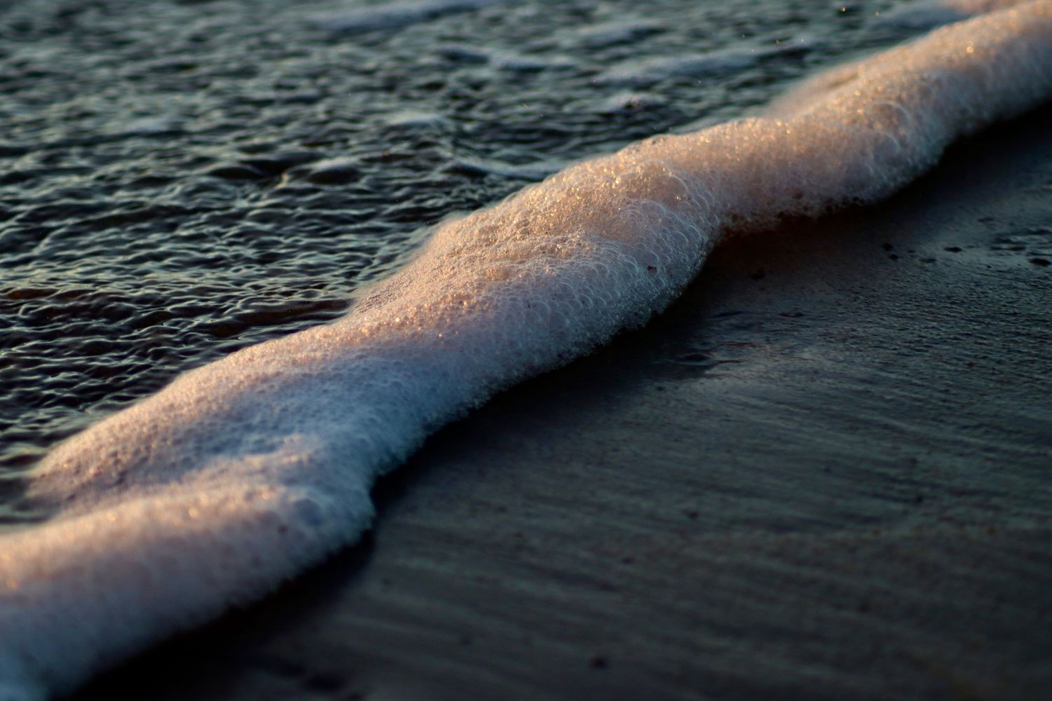 Waves roll in with white foam creating a line along the dark ocean surface.