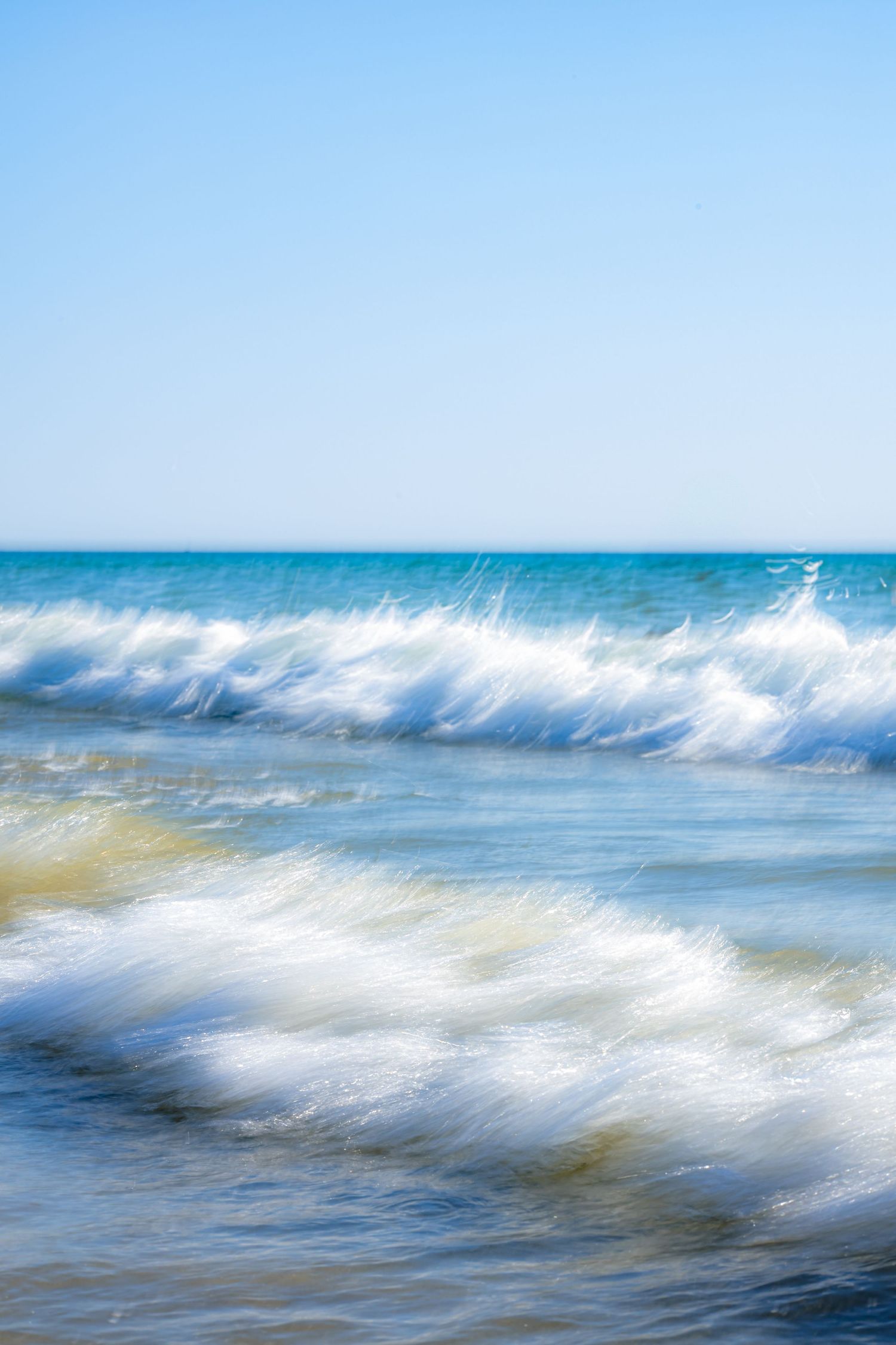 Waves crash and roll with white foam across a blue ocean surface creating a dynamic seascape pattern.