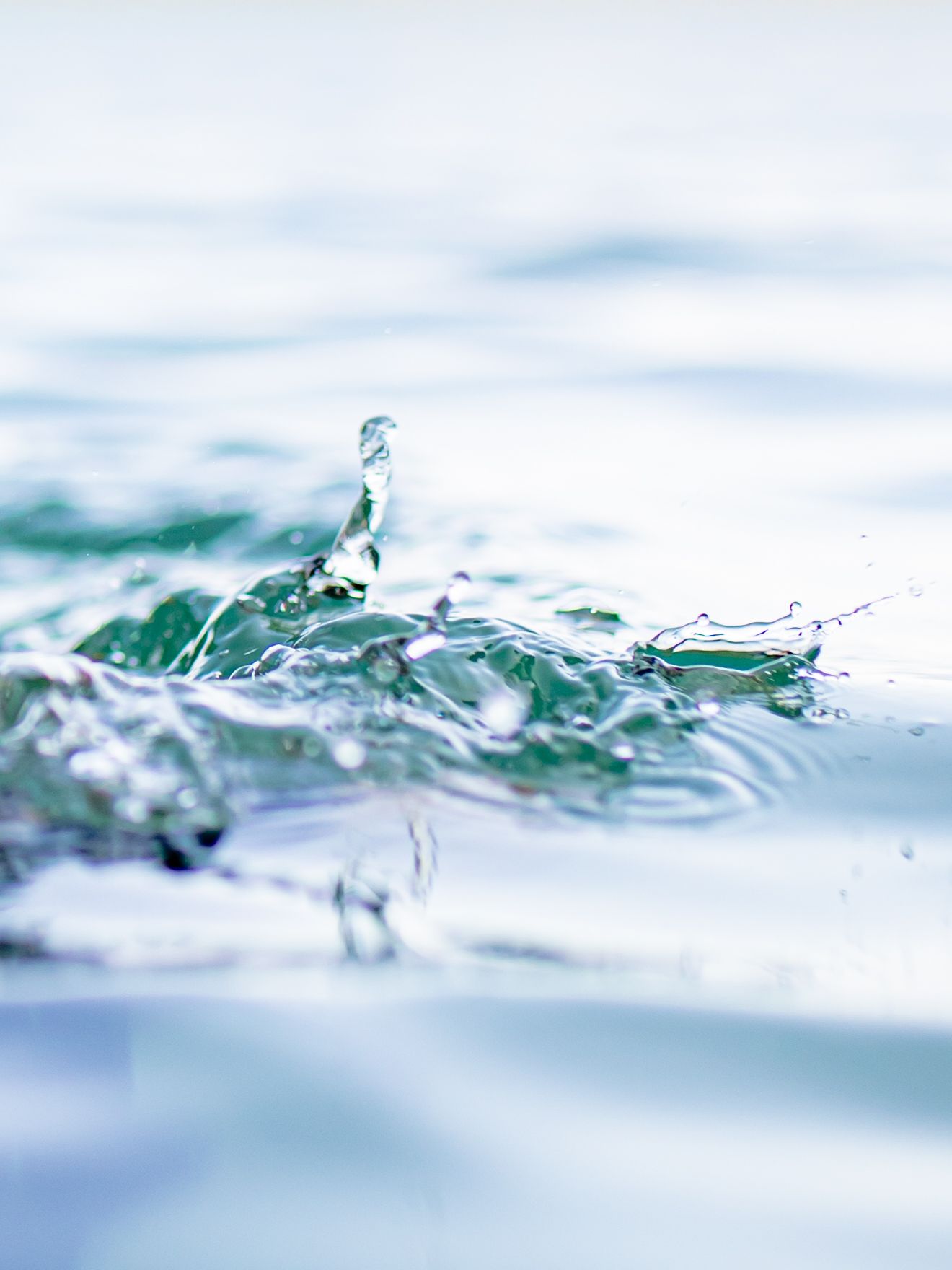 Close-up macro photograph of crystal clear water droplet splashing on turquoise water surface with soft focus background.