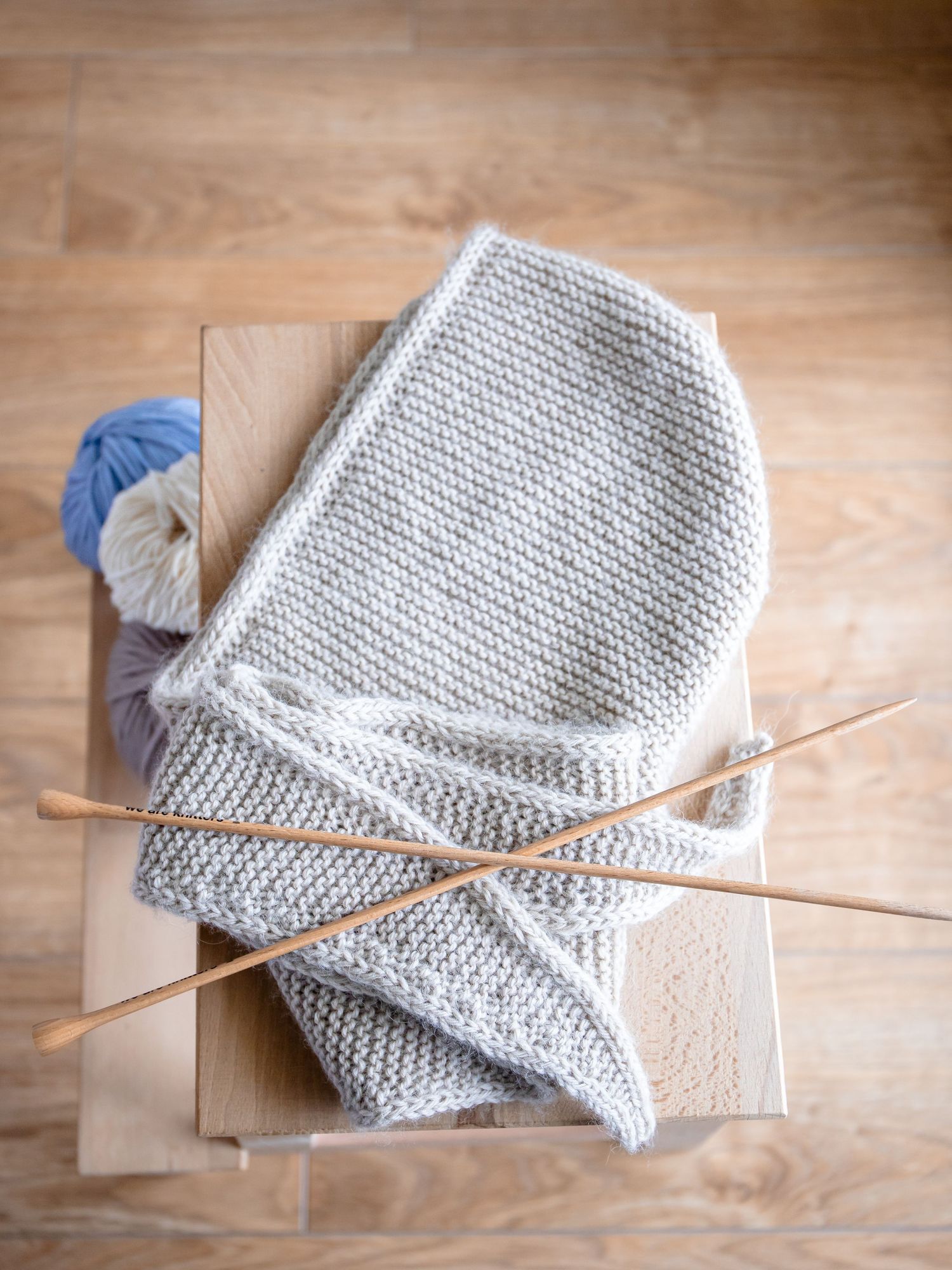 Light gray knitted textile with wooden knitting needles on craft paper surface.