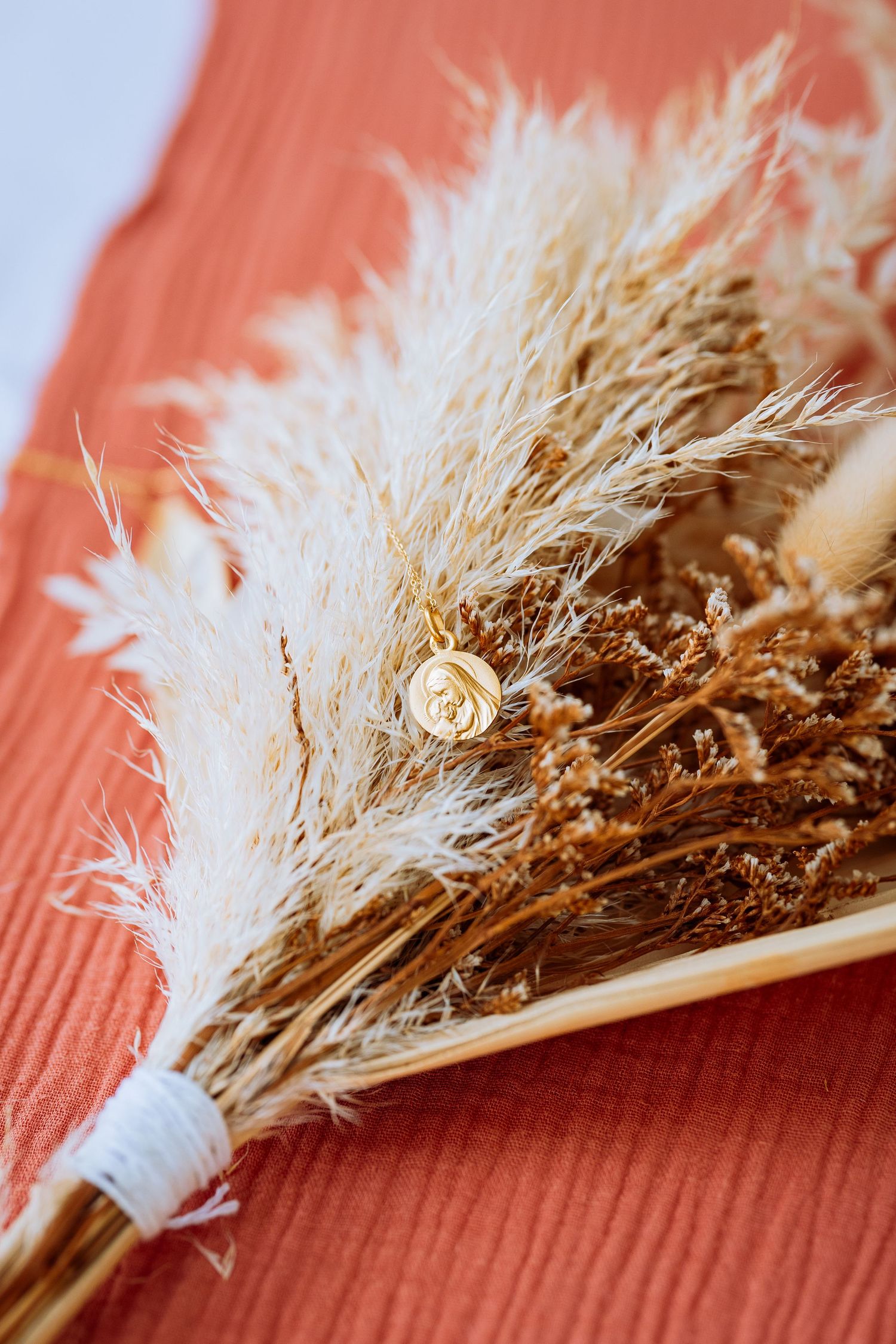 A delicate dried flower bouquet with pampas grass and a single cream rose tied together on a coral background.