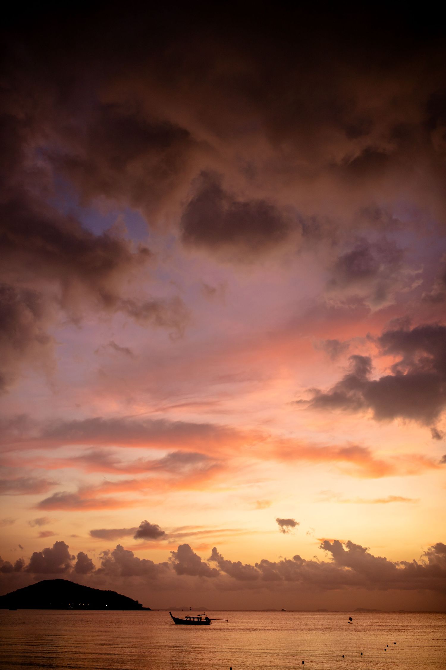 Dramatic sunset sky with pink and orange clouds over silhouetted islands and a small boat.
