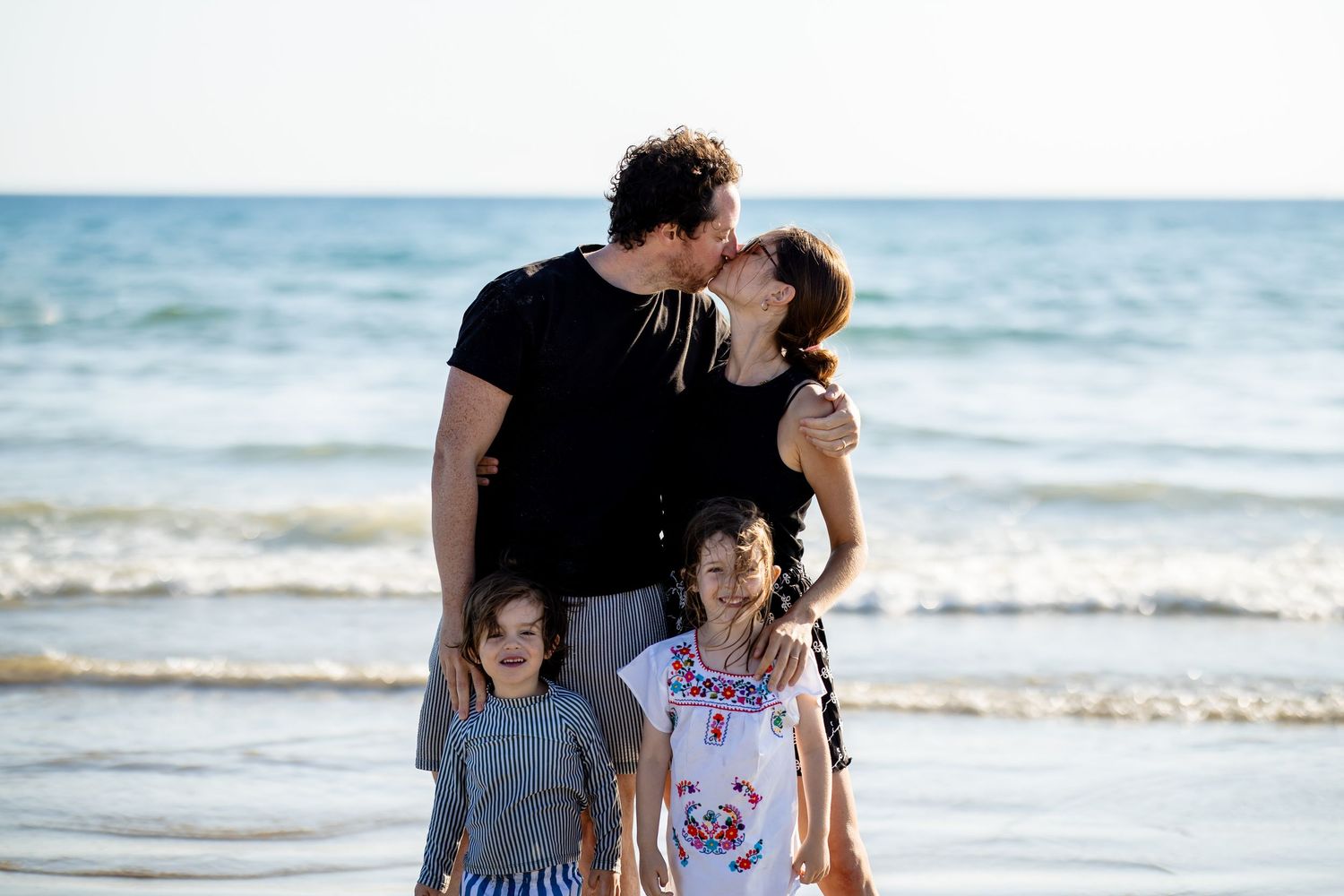 Family shares tender moments together while walking along a scenic beach at sunset.