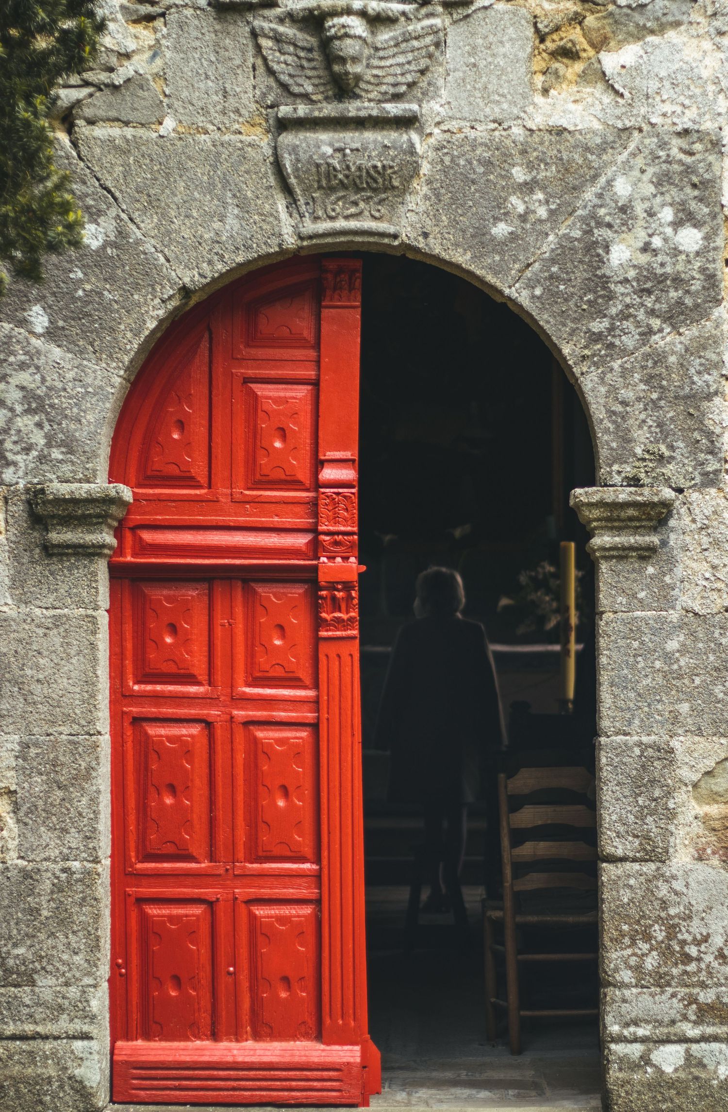 Red arched doors with ornate panels set in an old stone church wall.