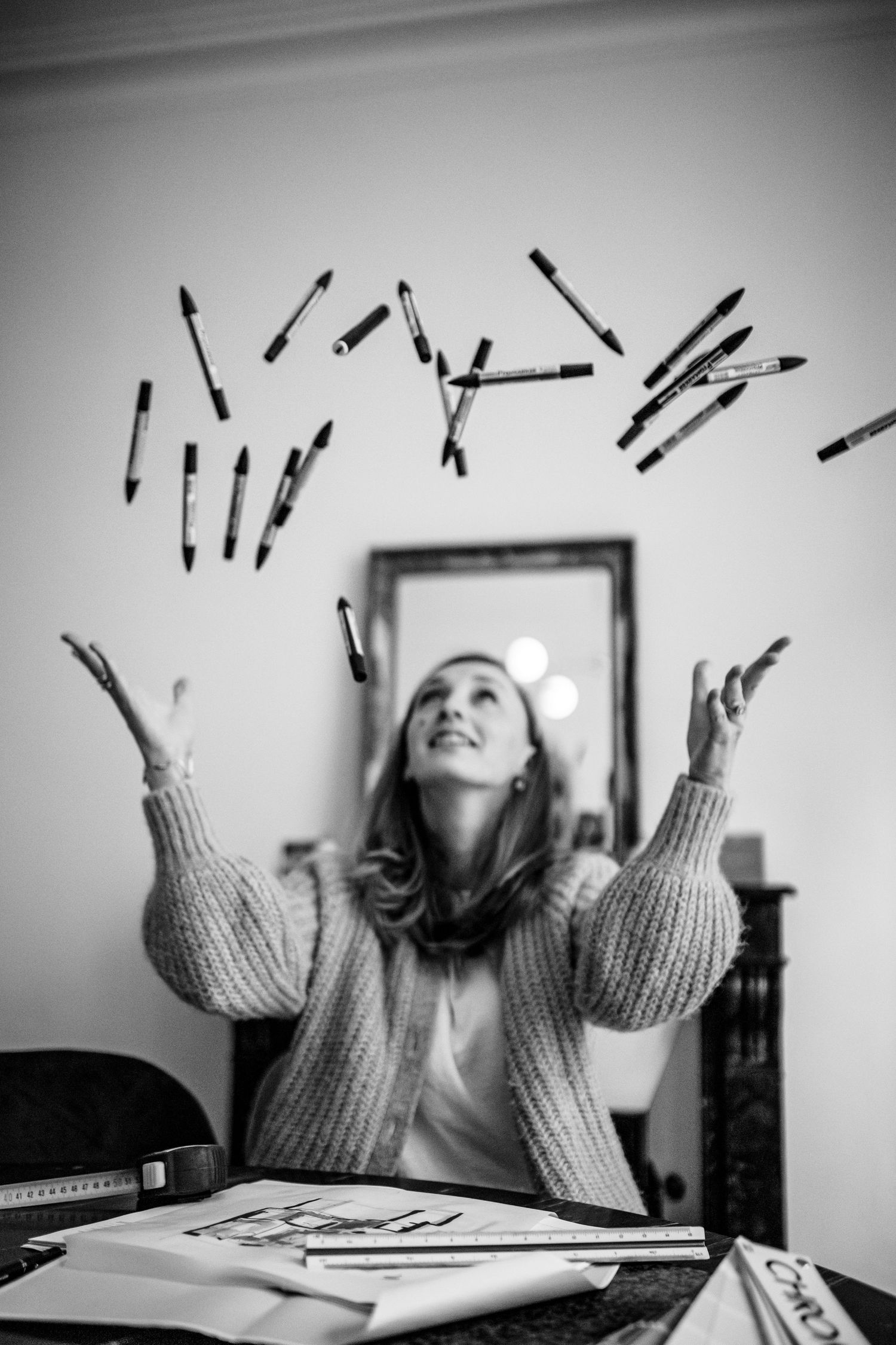 Creative black and white image of pens being tossed in the air above a desk.