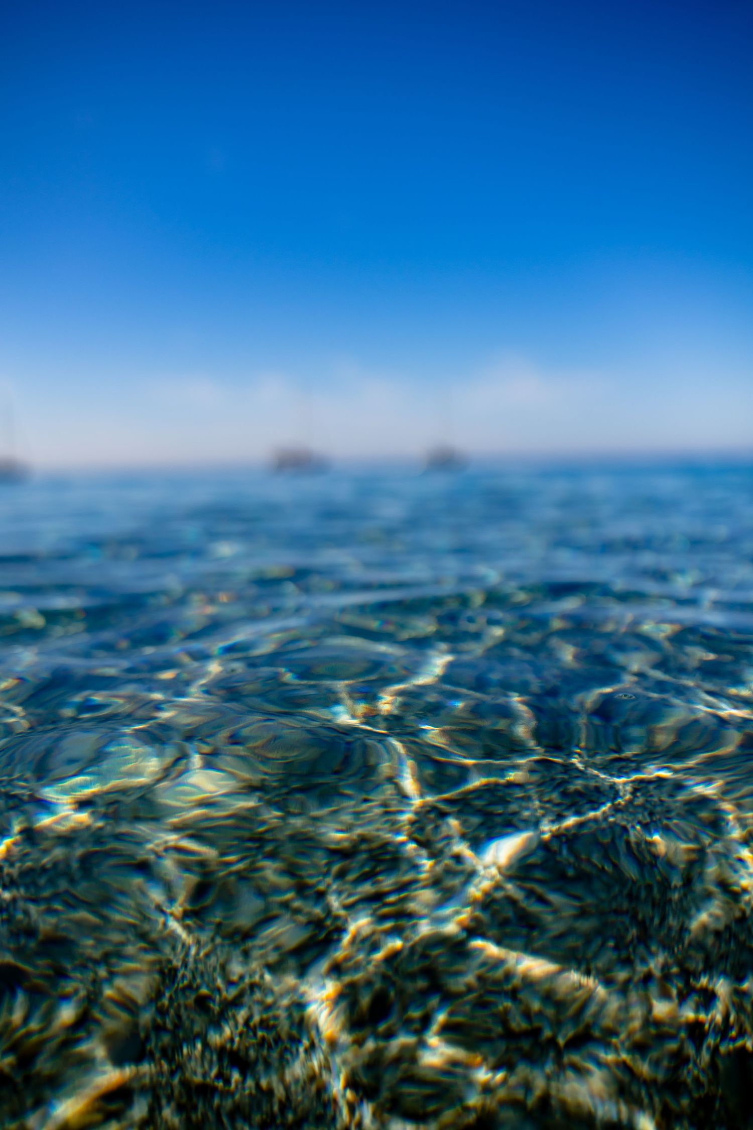 Underwater view of crystal clear ocean water with rippling surface and deep blue sky above on a sunny day.
