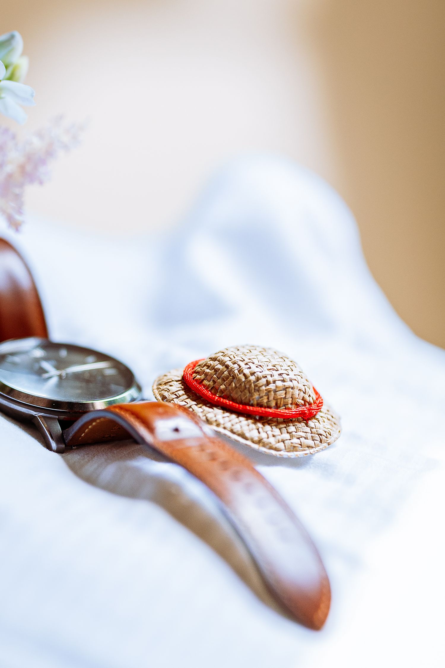 Decorative straw hat with red ribbon band photographed in sequence on white fabric with soft focus and shallow depth of field.