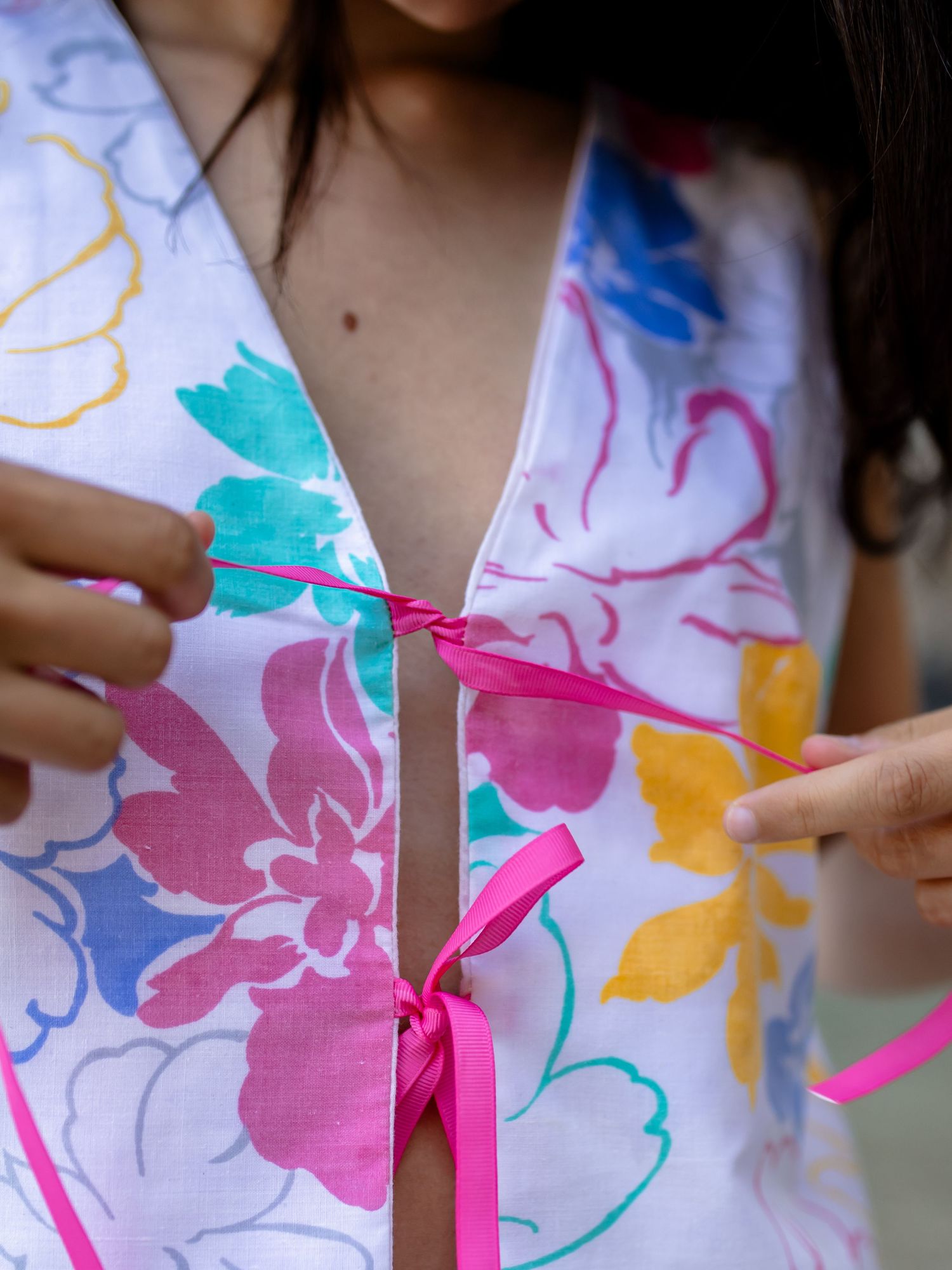 Close-up view of hands fastening a pink ribbon on a colorful floral print dress.