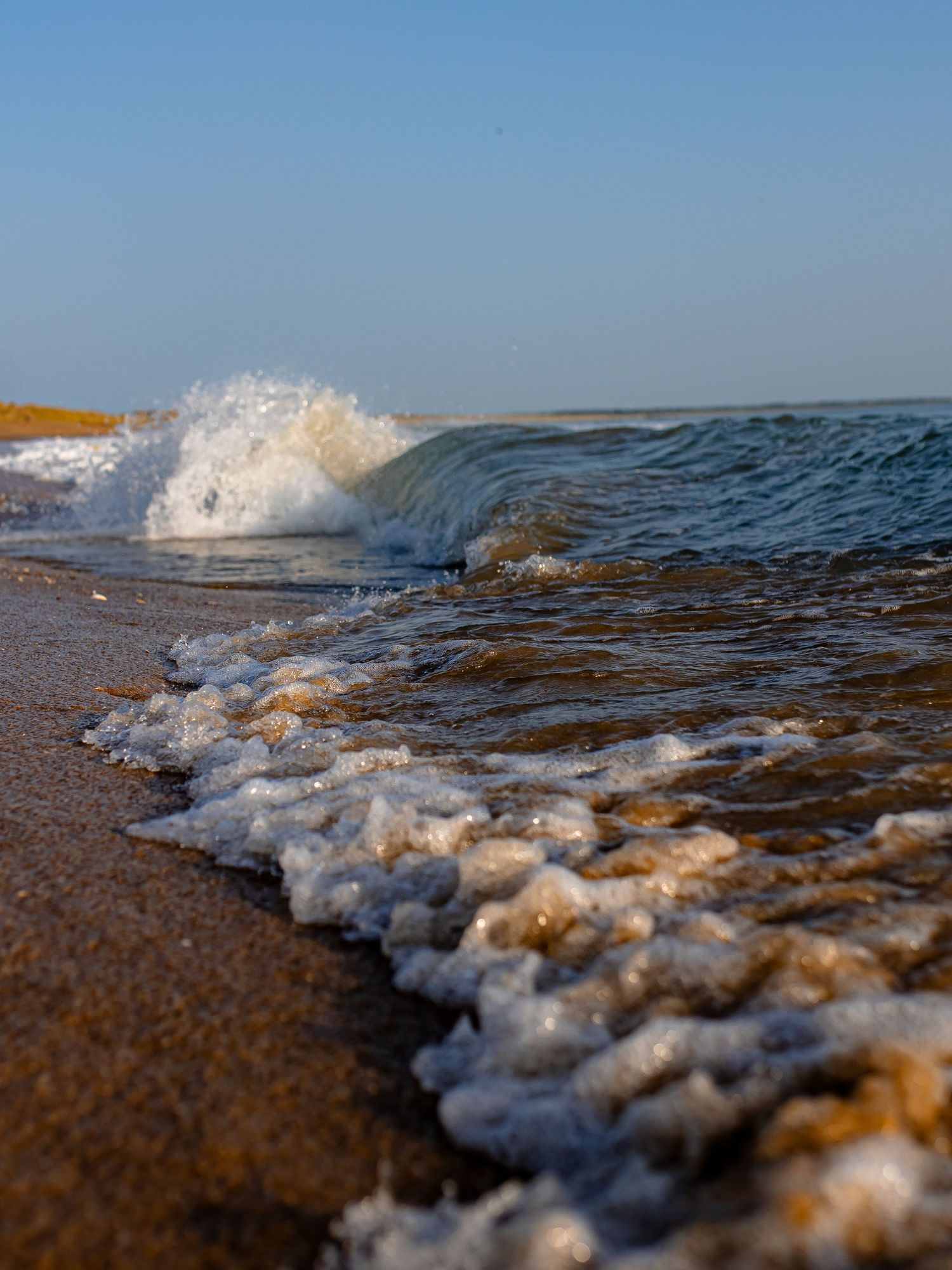 Sequence of waves crashing onto a sandy beach shore with white foam and blue ocean water in golden sunlight.