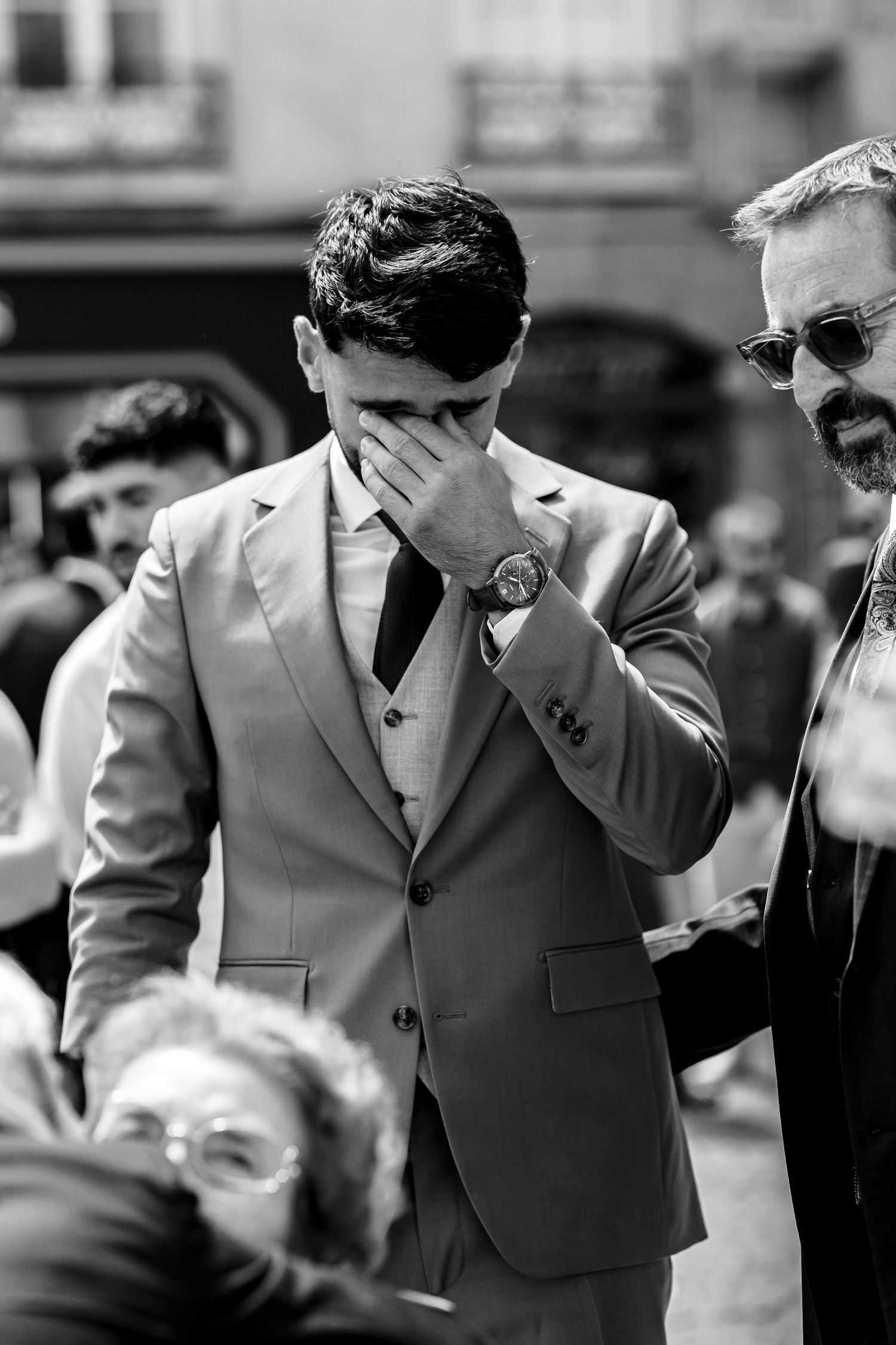 Black and white photo of emotional groom covering his face during outdoor wedding ceremony.