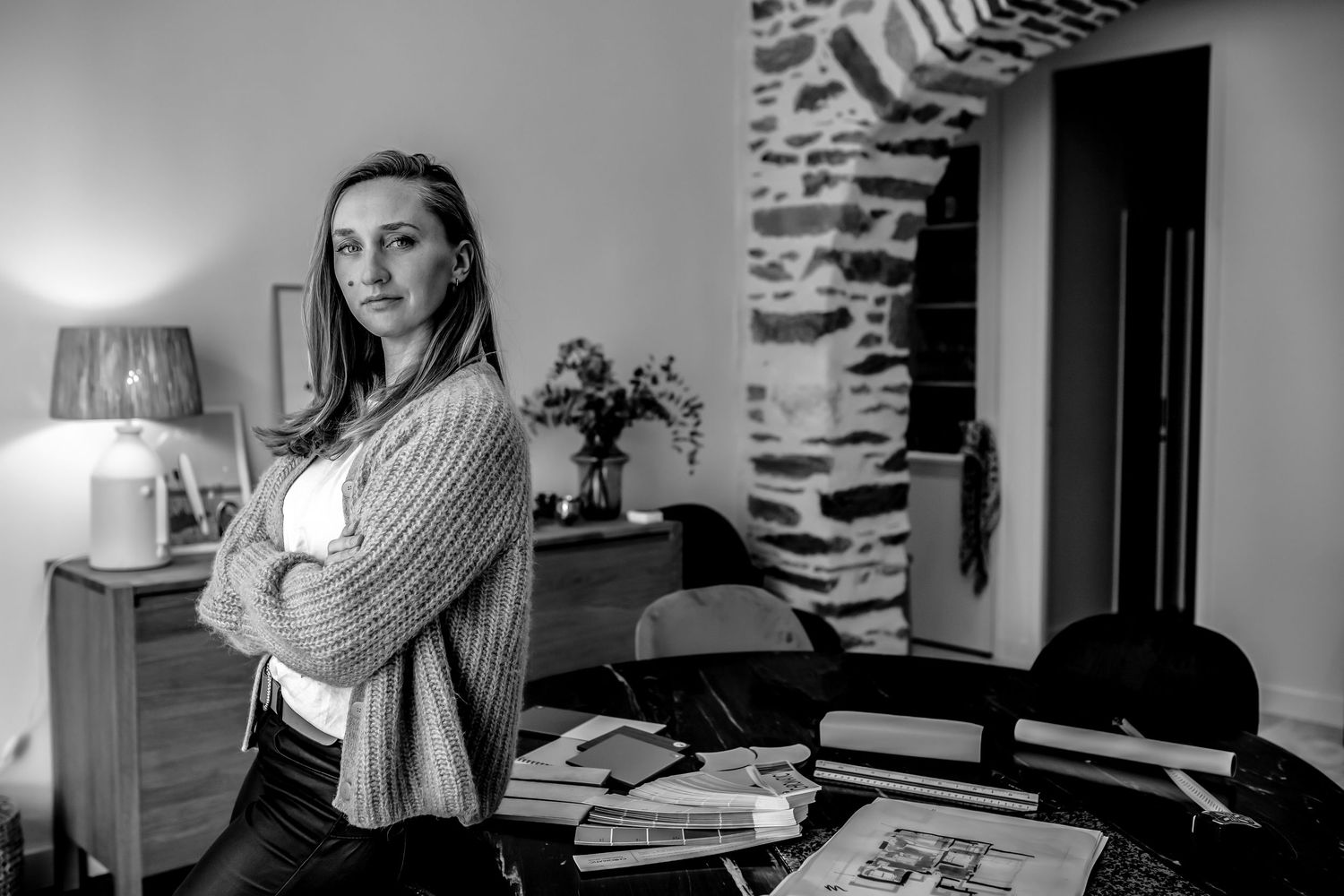 Black and white photo of someone standing confidently in an office with stone walls and books.