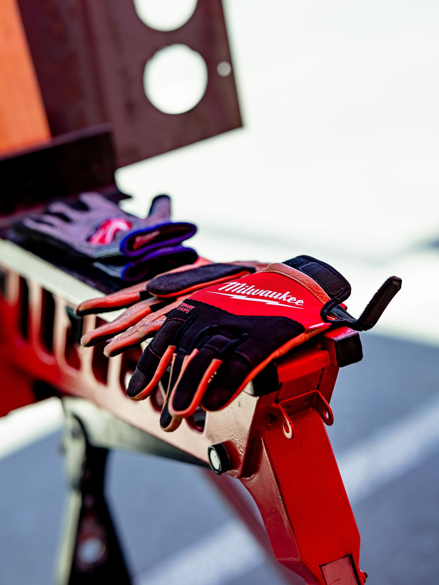 Red and black Milwaukee work gloves resting on metal equipment.