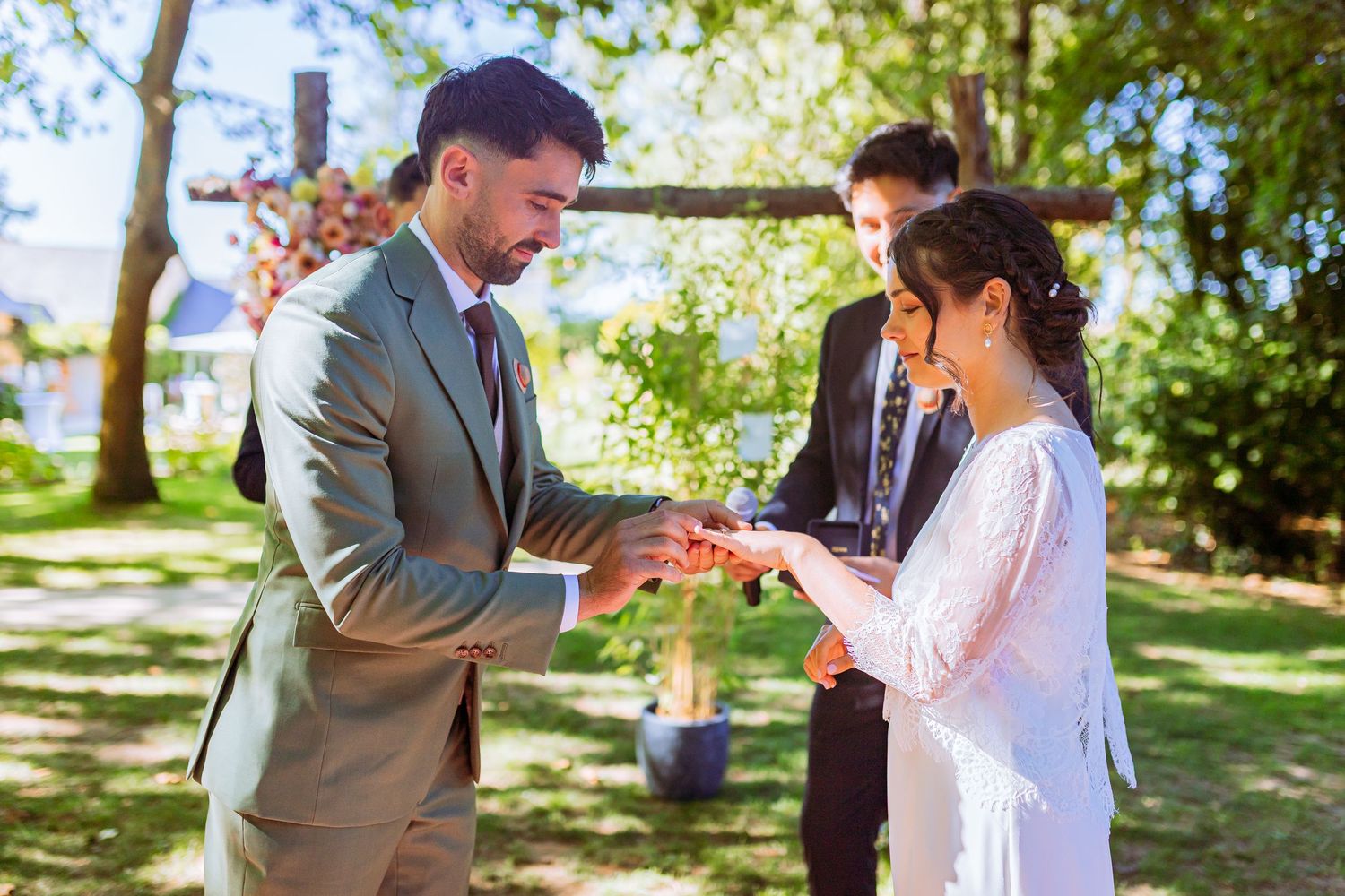 A couple shares a romantic moment during their outdoor wedding ceremony in a sunlit garden setting.