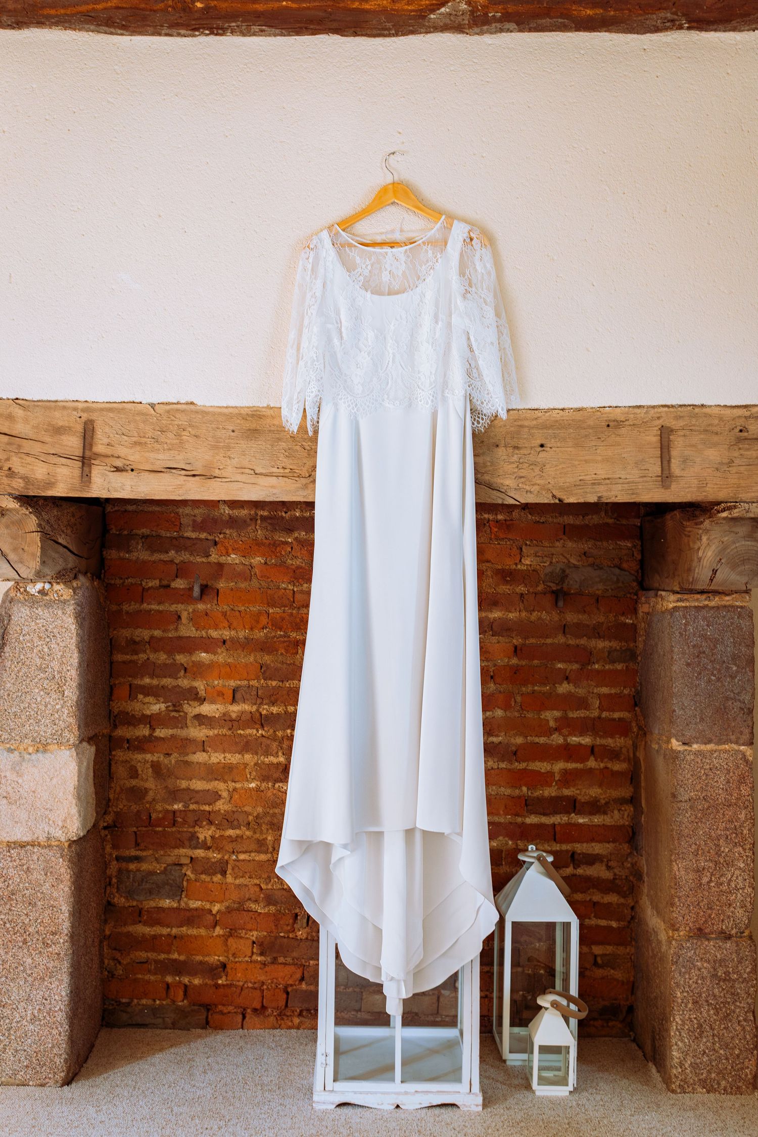 White linen dresses displayed on minimalist stands against rustic brick wall in vintage interior setting.