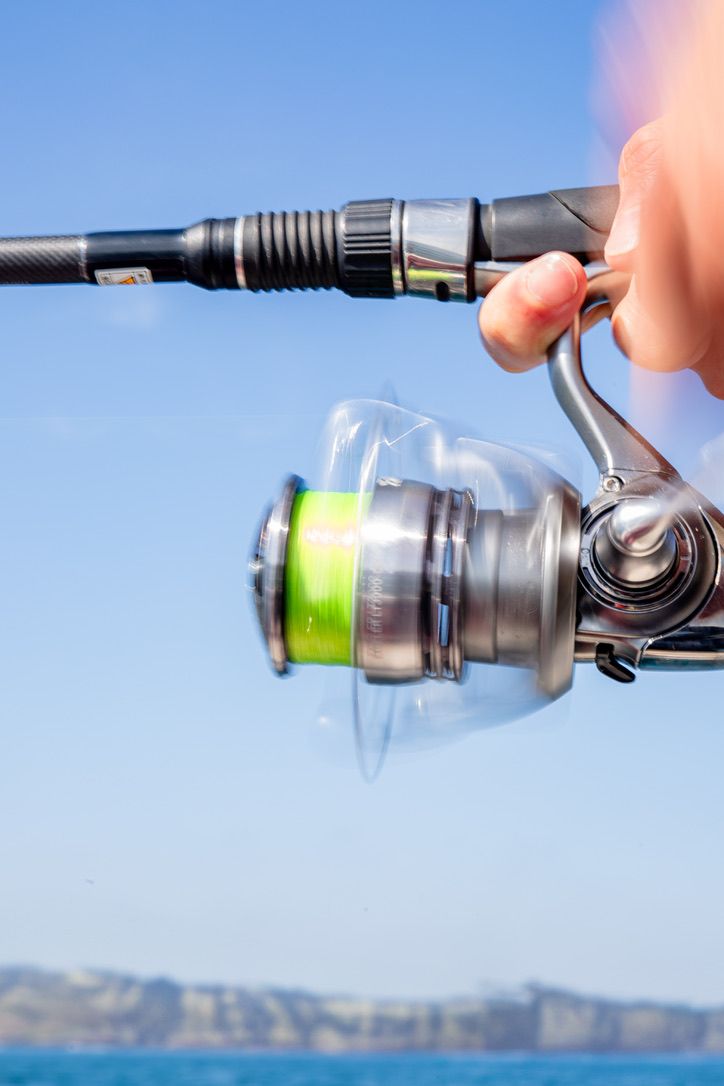 Fishing reel in action against blue sky and coastal background.