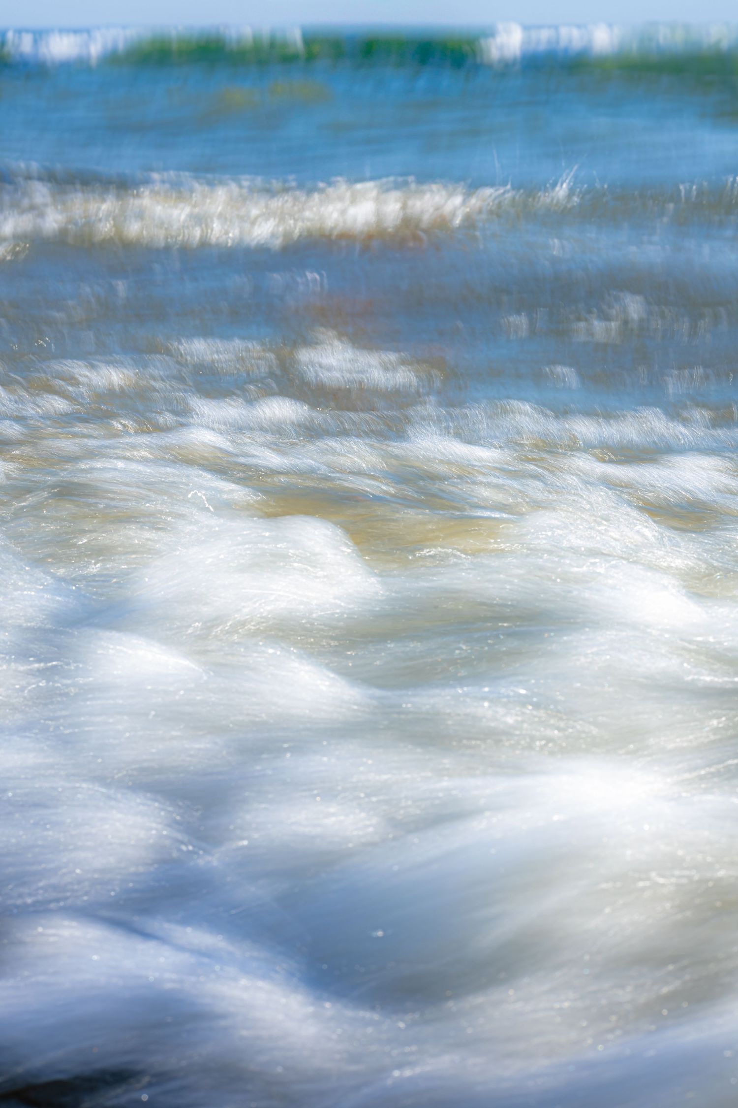 Abstract blurred motion of ocean waves creating a dreamy blue and white pattern in sunlight.