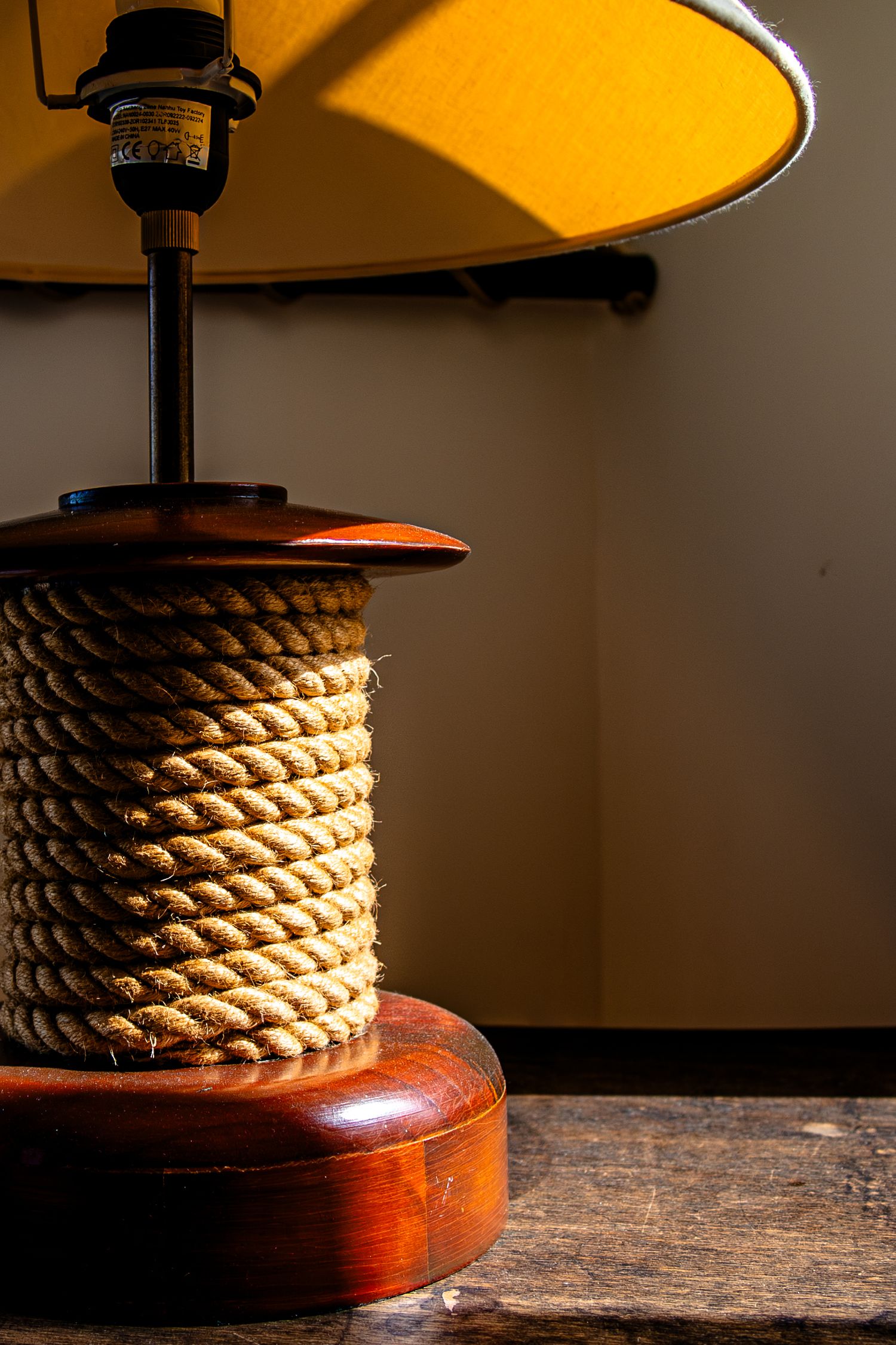 Vintage table lamp with rope-wrapped base and wooden pedestal casts warm glow against dark background.