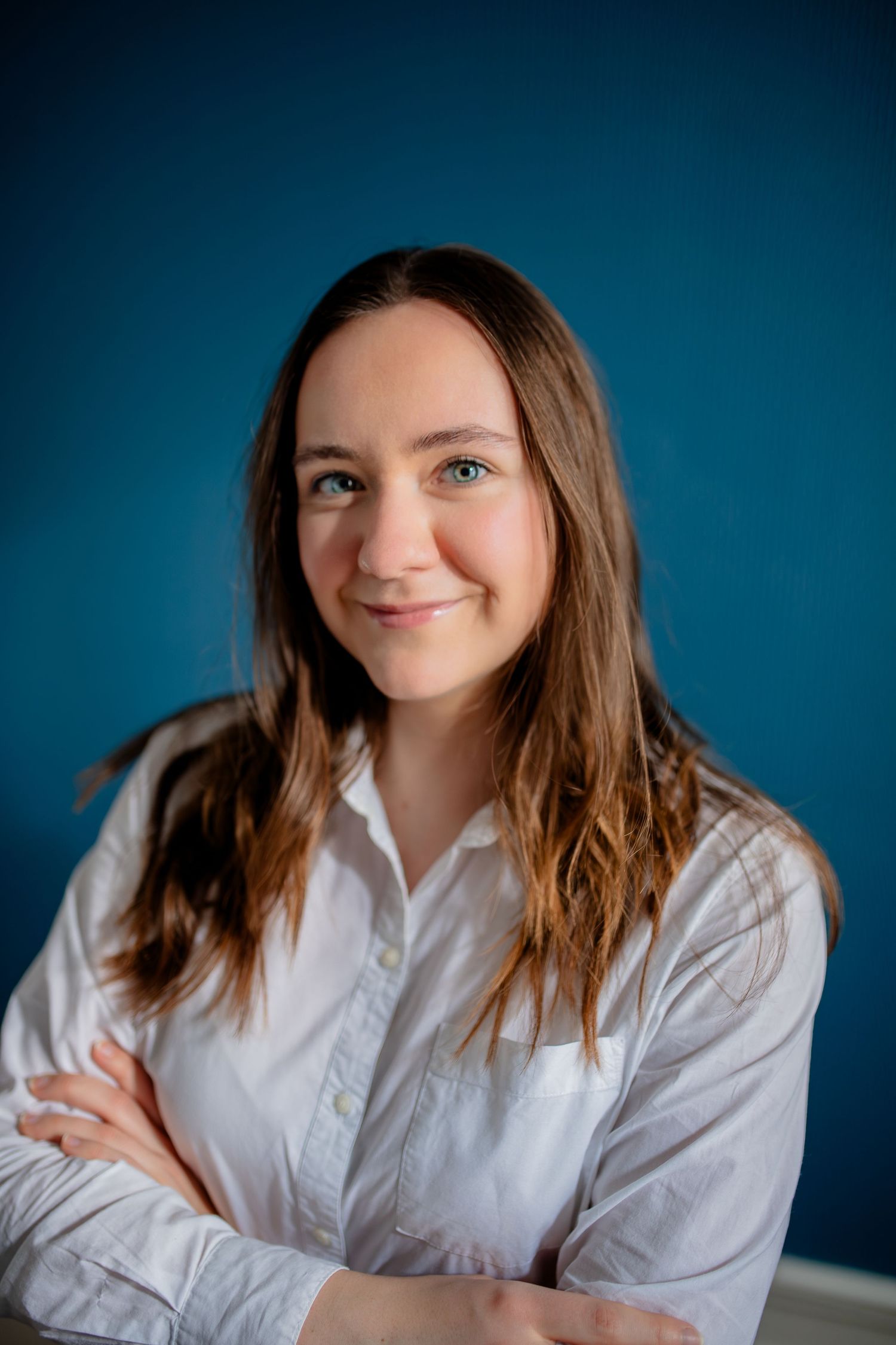 Business portrait in white shirt with crossed arms against dark blue backdrop.