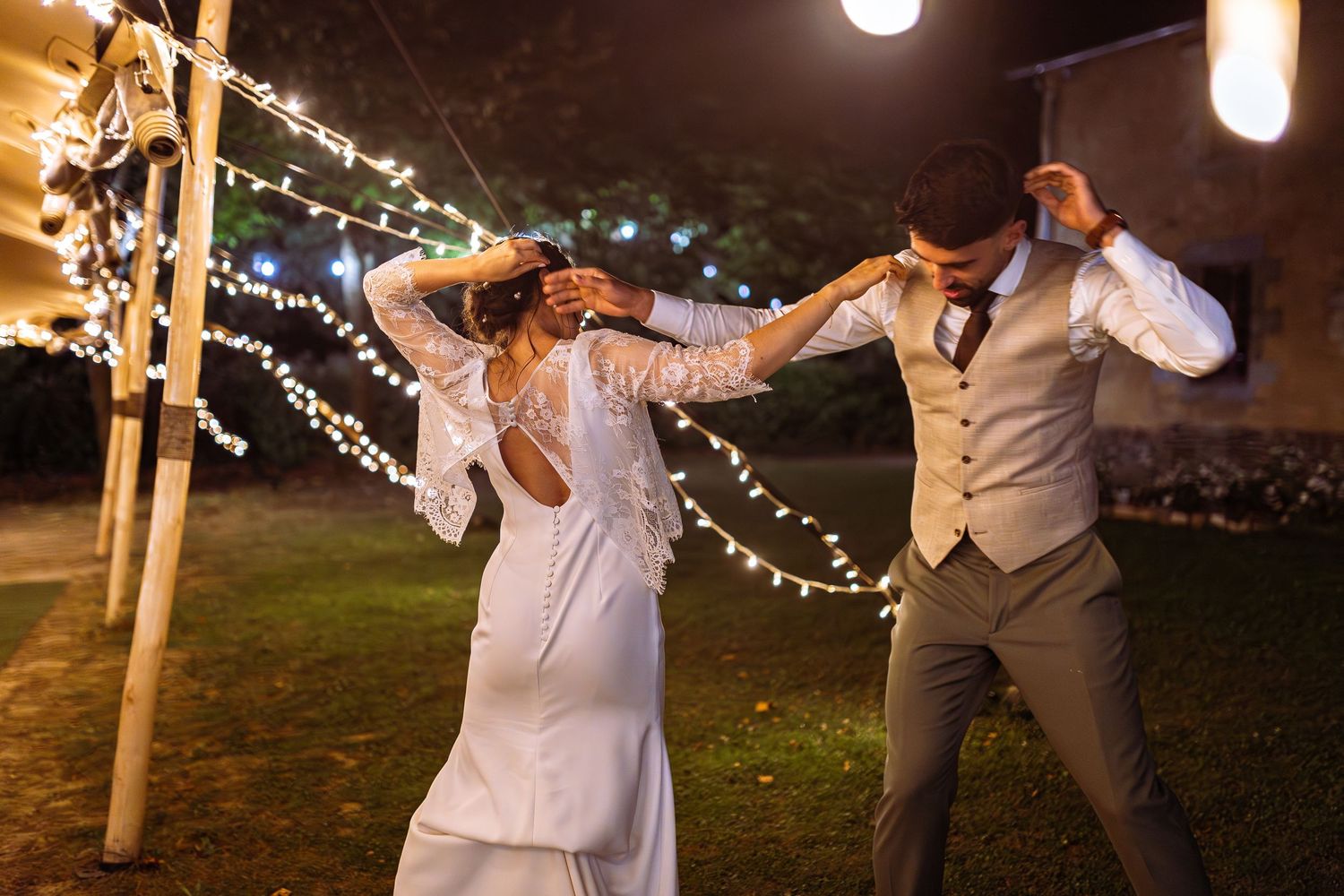 Wedding guests dance together under string lights during an outdoor evening celebration.