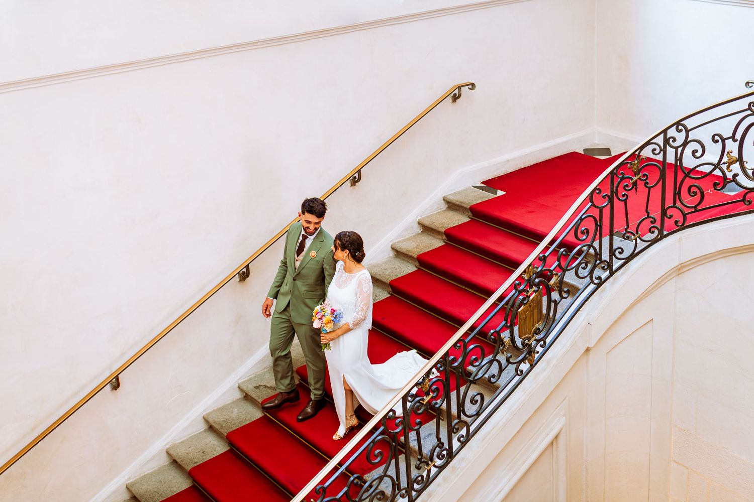 Elegant red carpeted staircase with ornate black iron railing and gold handrail in a luxury interior setting.