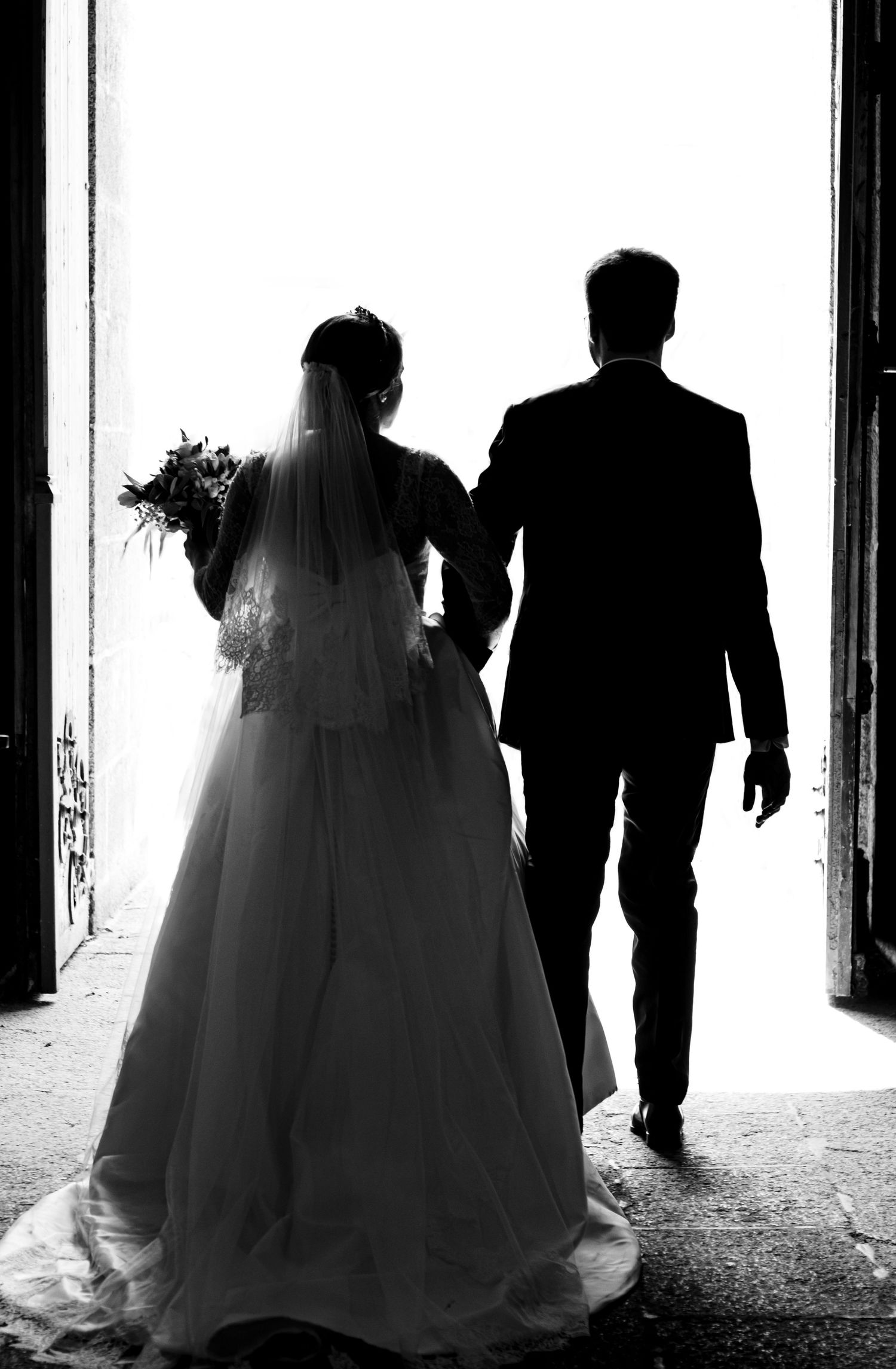 Silhouettes of a wedding couple walking together through a bright corridor.