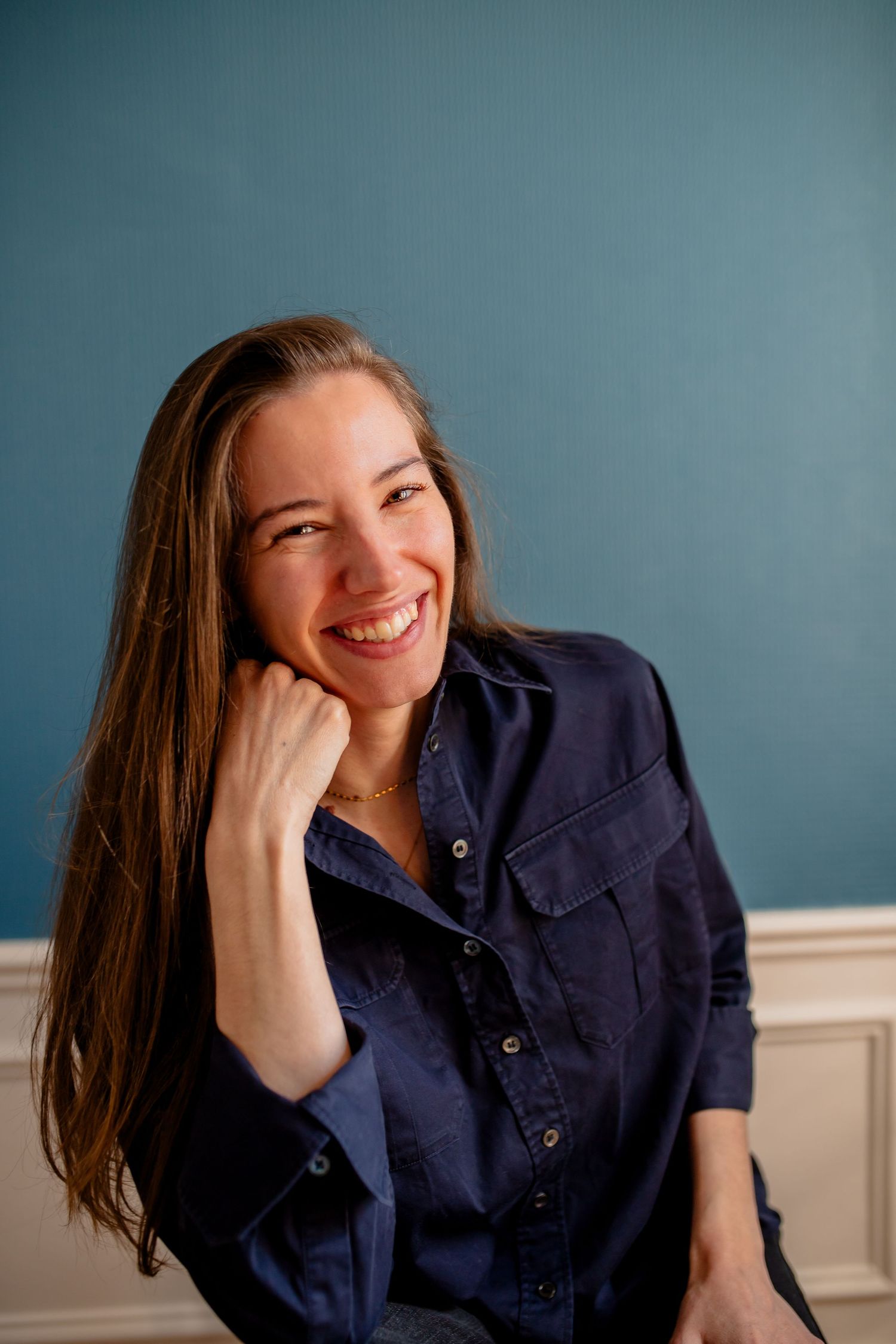 Candid laughing portrait against blue wall wearing dark button-up shirt.