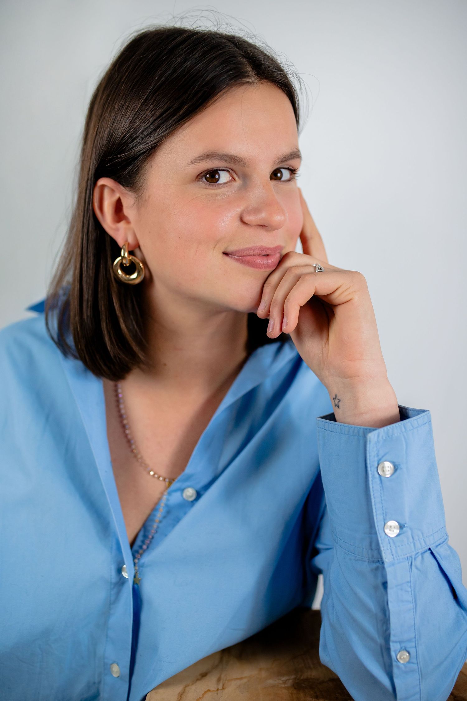A person in a light blue button-down shirt poses thoughtfully against a white background.