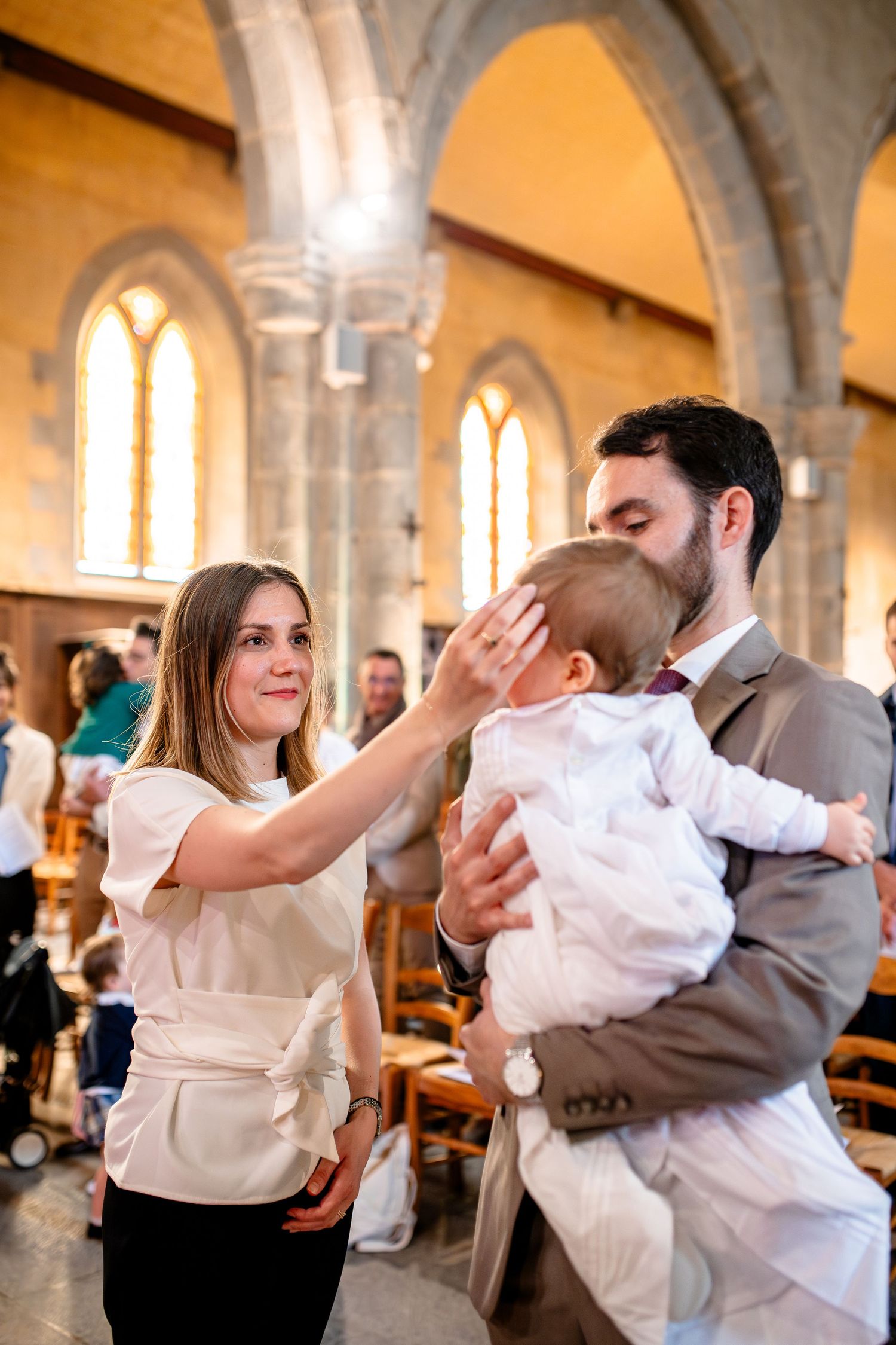 A family shares a tender moment during a christening ceremony inside a historic stone church with arched windows.