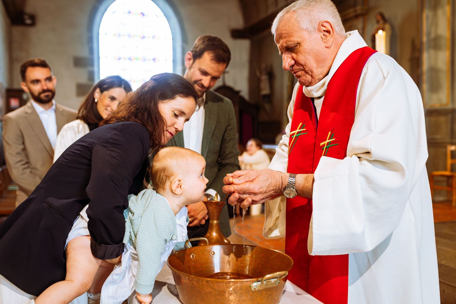A baptismal ceremony takes place in a church as a priest performs the religious sacrament on a baby.