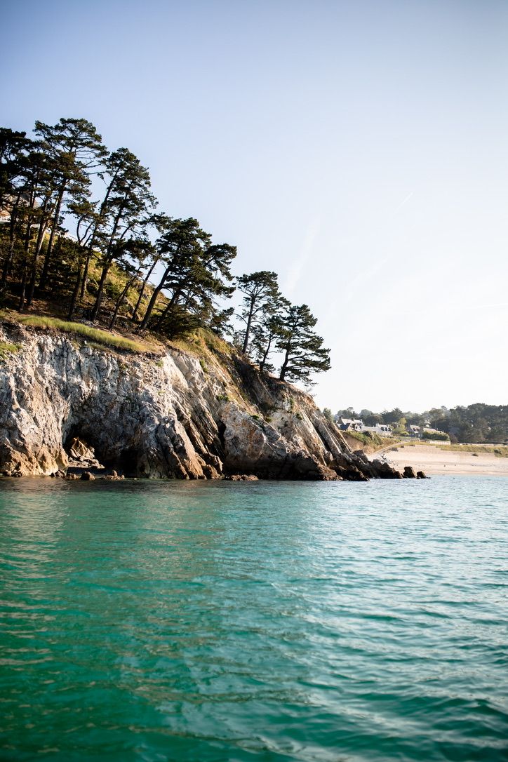 Rocky coastal cliffs with pine trees overlooking turquoise waters.