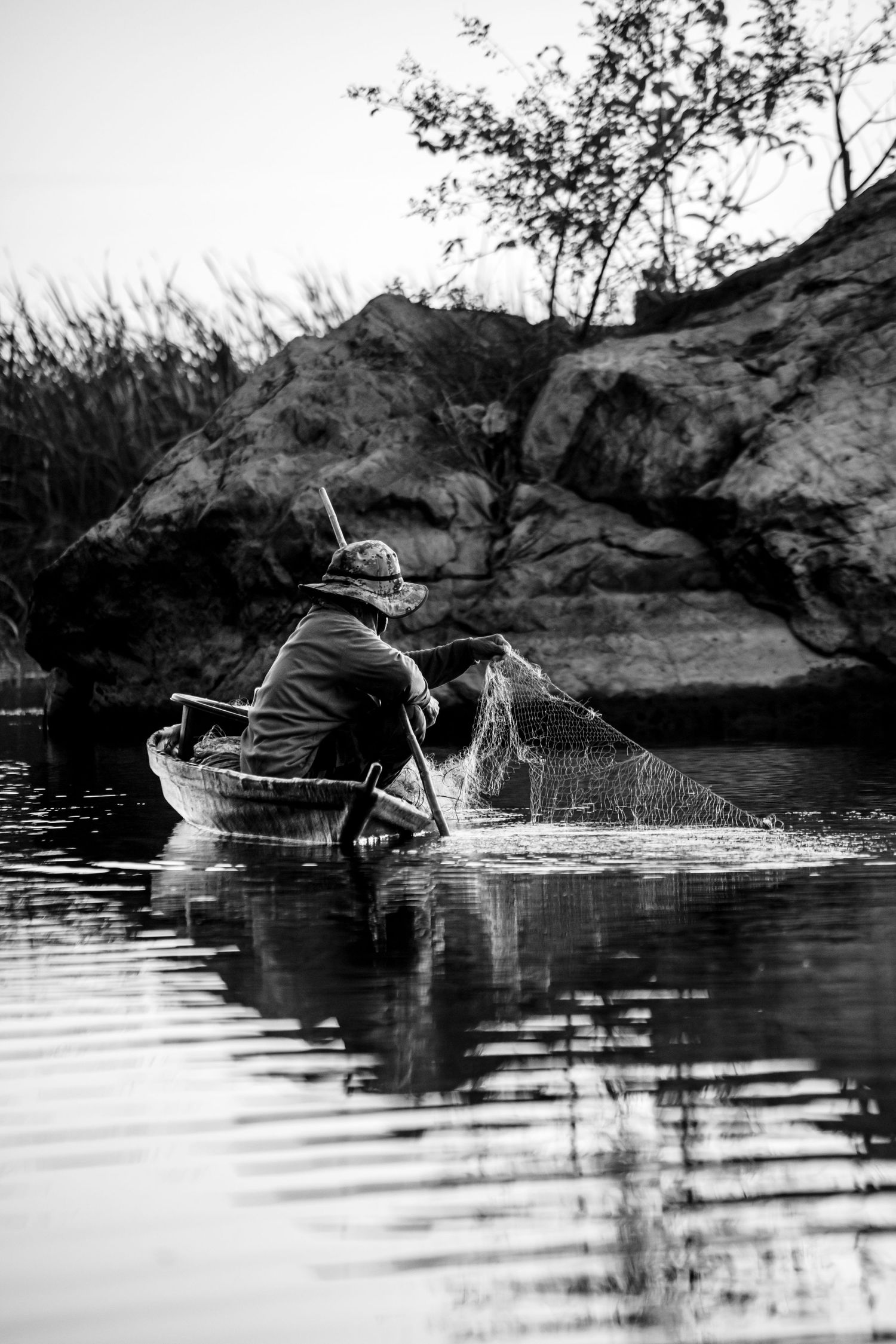 Fisherman casting nets in silhouette against reflective water at dusk.