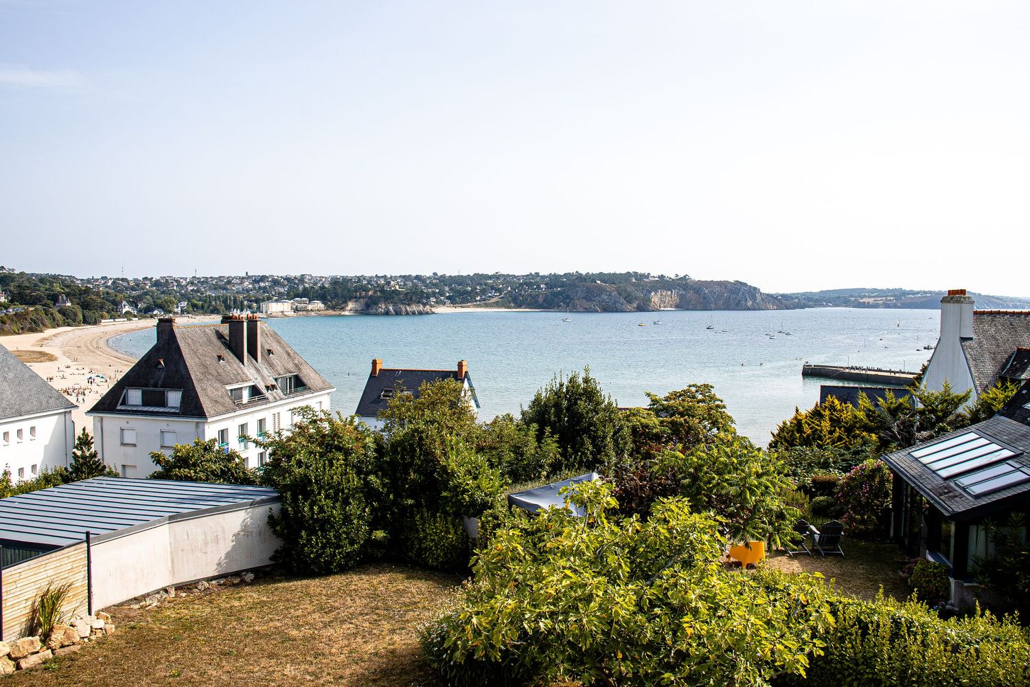 Scenic coastal panorama with waterfront homes and lush greenery overlooking a tranquil bay on a sunny day.
