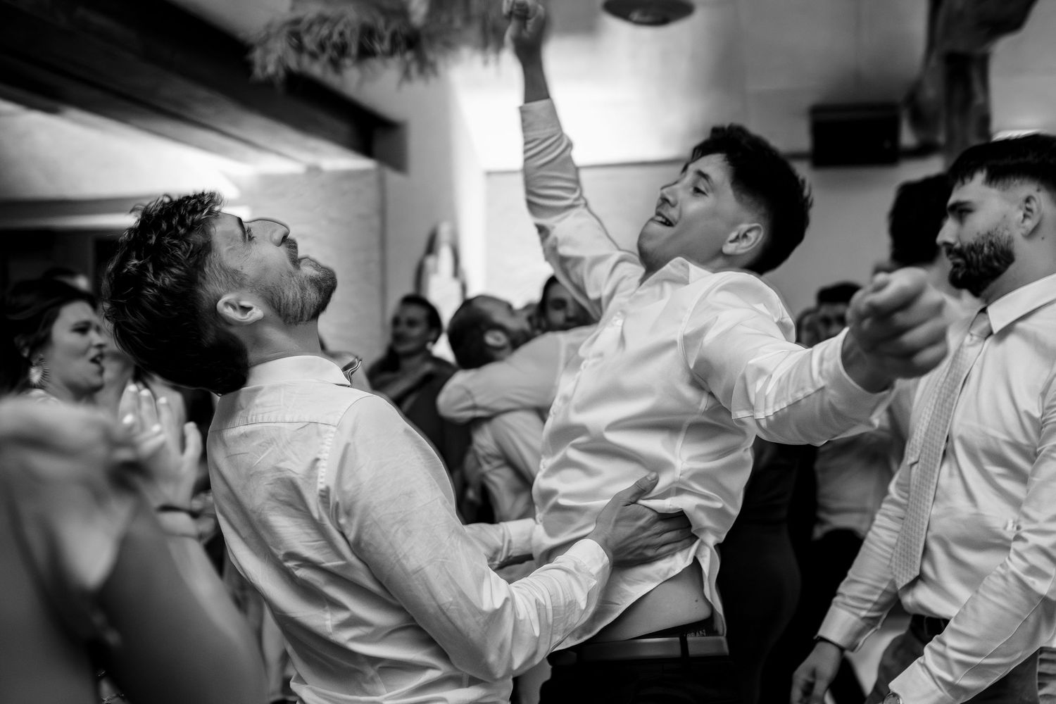 A series of candid black and white photos showing wedding guests dancing and celebrating at a reception party.