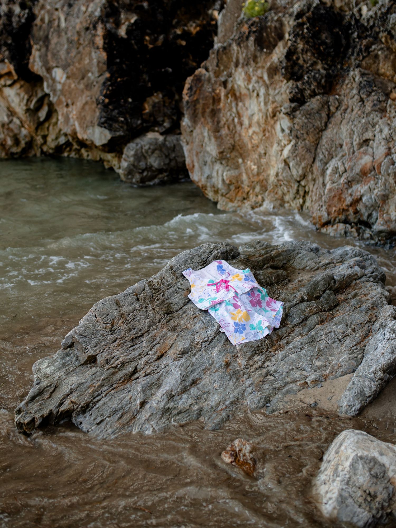 A white paper with colorful markings gets swept away by rushing water against rocky terrain.