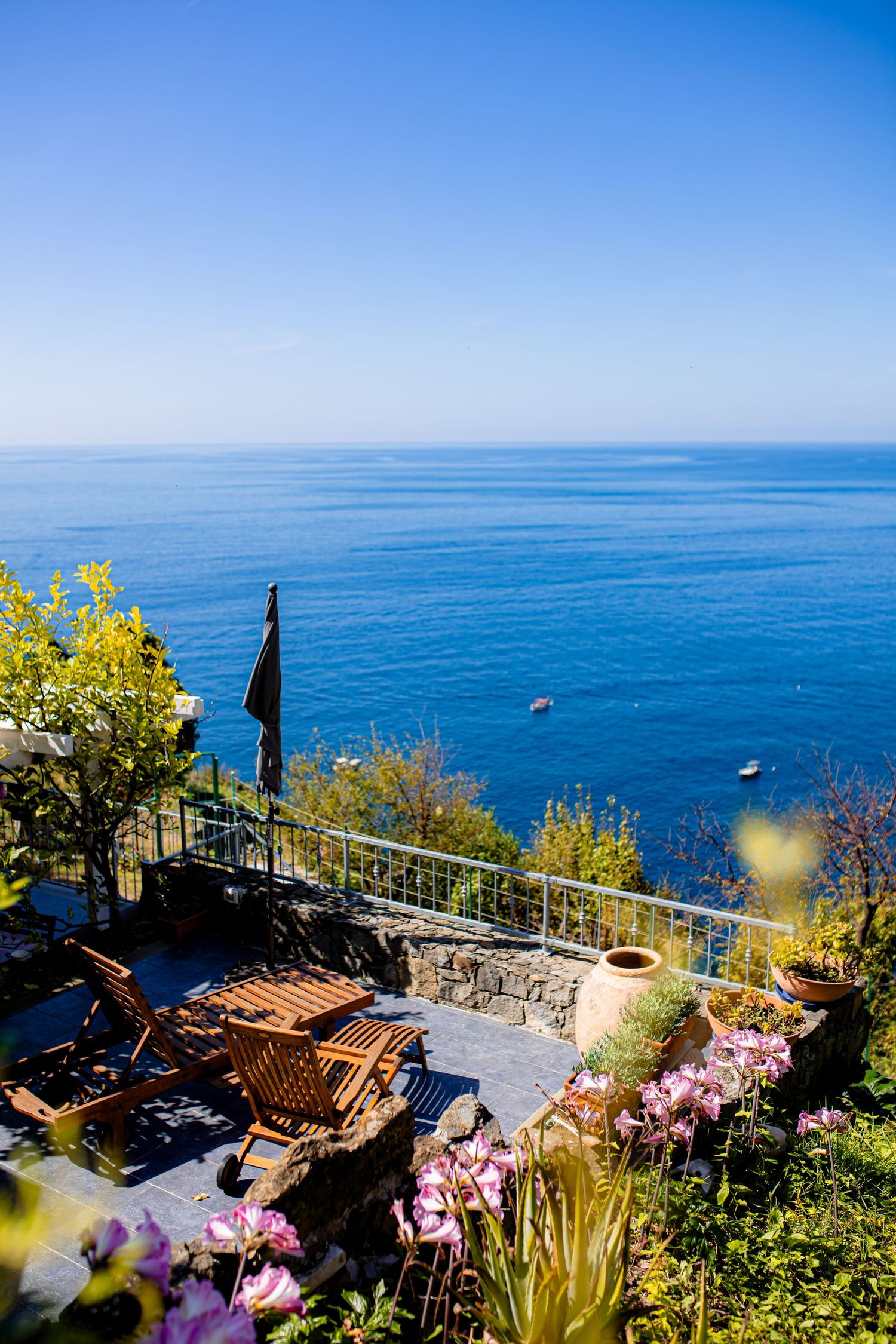 Scenic Mediterranean coastal terrace with blooming flowers and panoramic ocean views from a hilltop restaurant.
