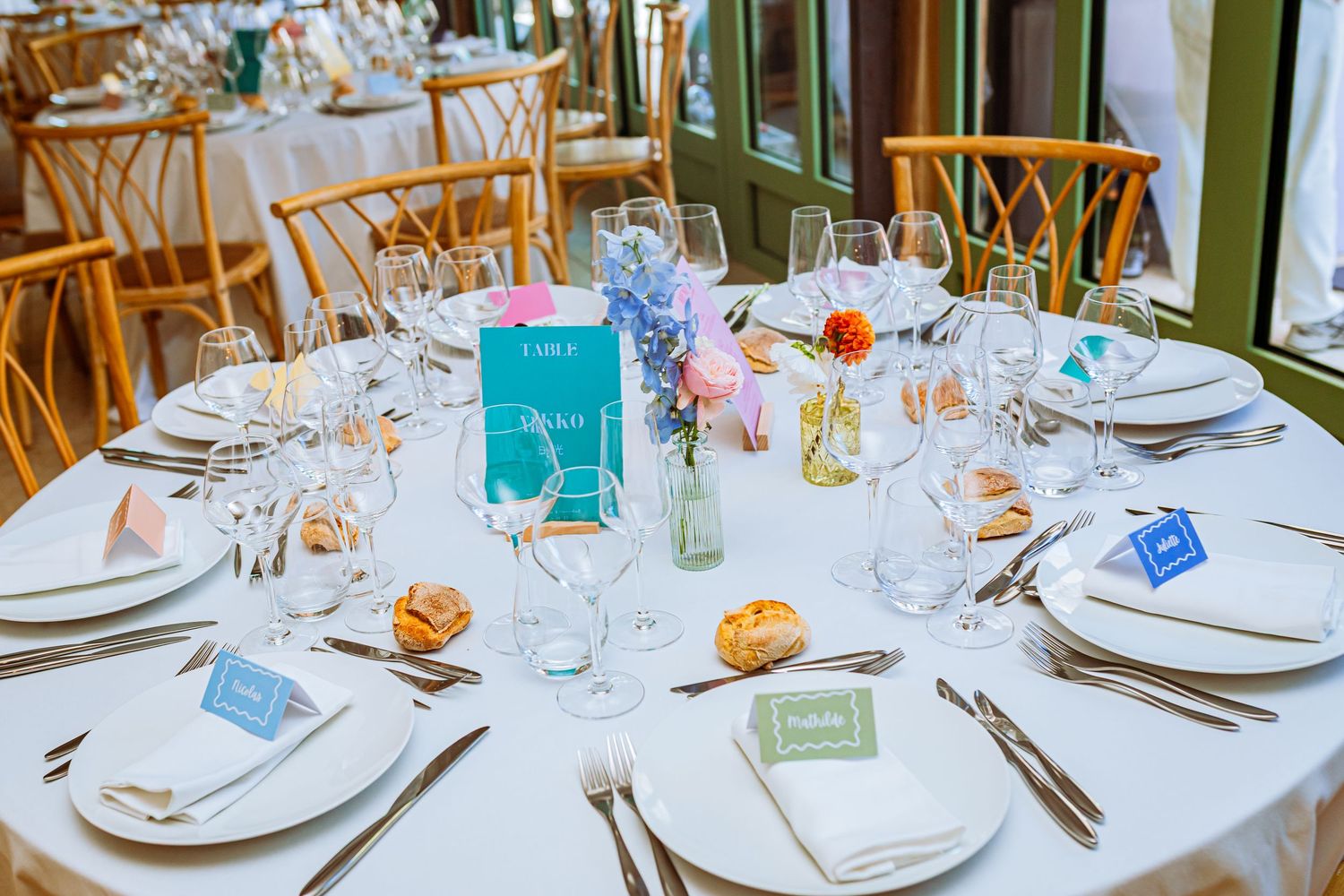 Elegant wedding reception tables set with white linens, glassware, and delicate floral centerpieces in a bright venue.