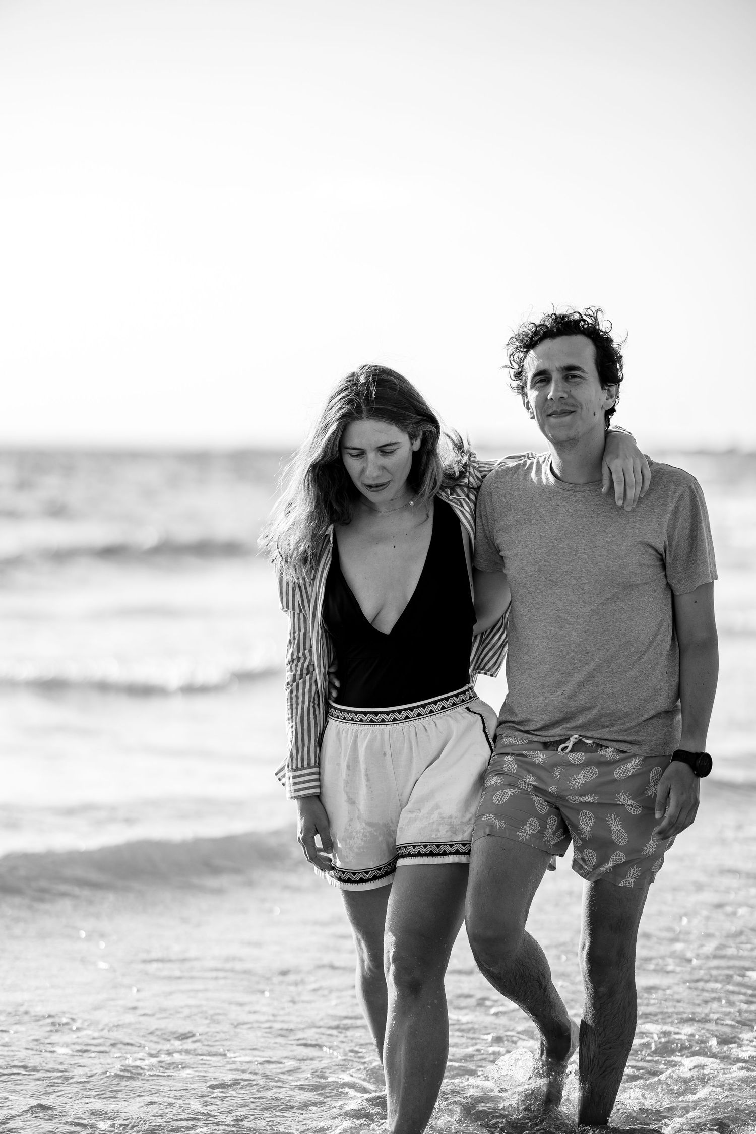 A couple walks together along the beach shoreline in black and white.